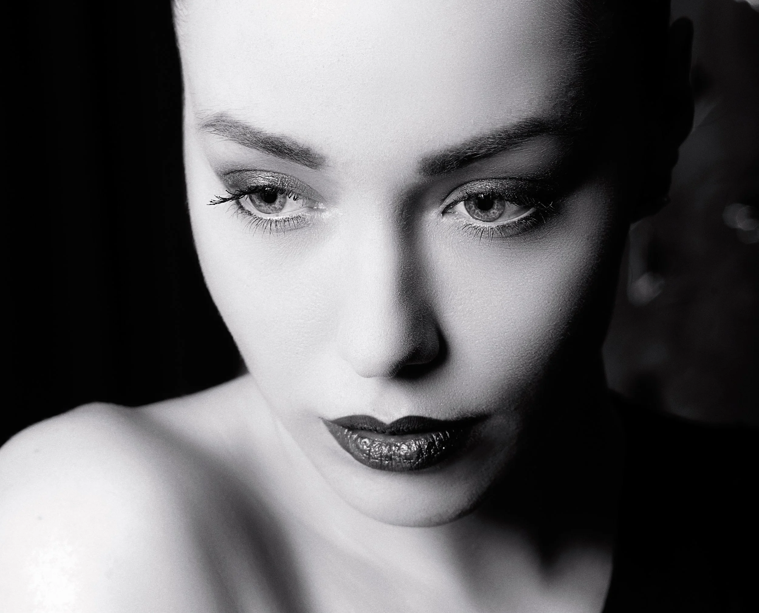 Un portrait en noir et blanc d'une femme avec un maquillage sophistiqué, très proche de la caméra pour accentuer ses yeux, ses sourcils et ses lèvres.