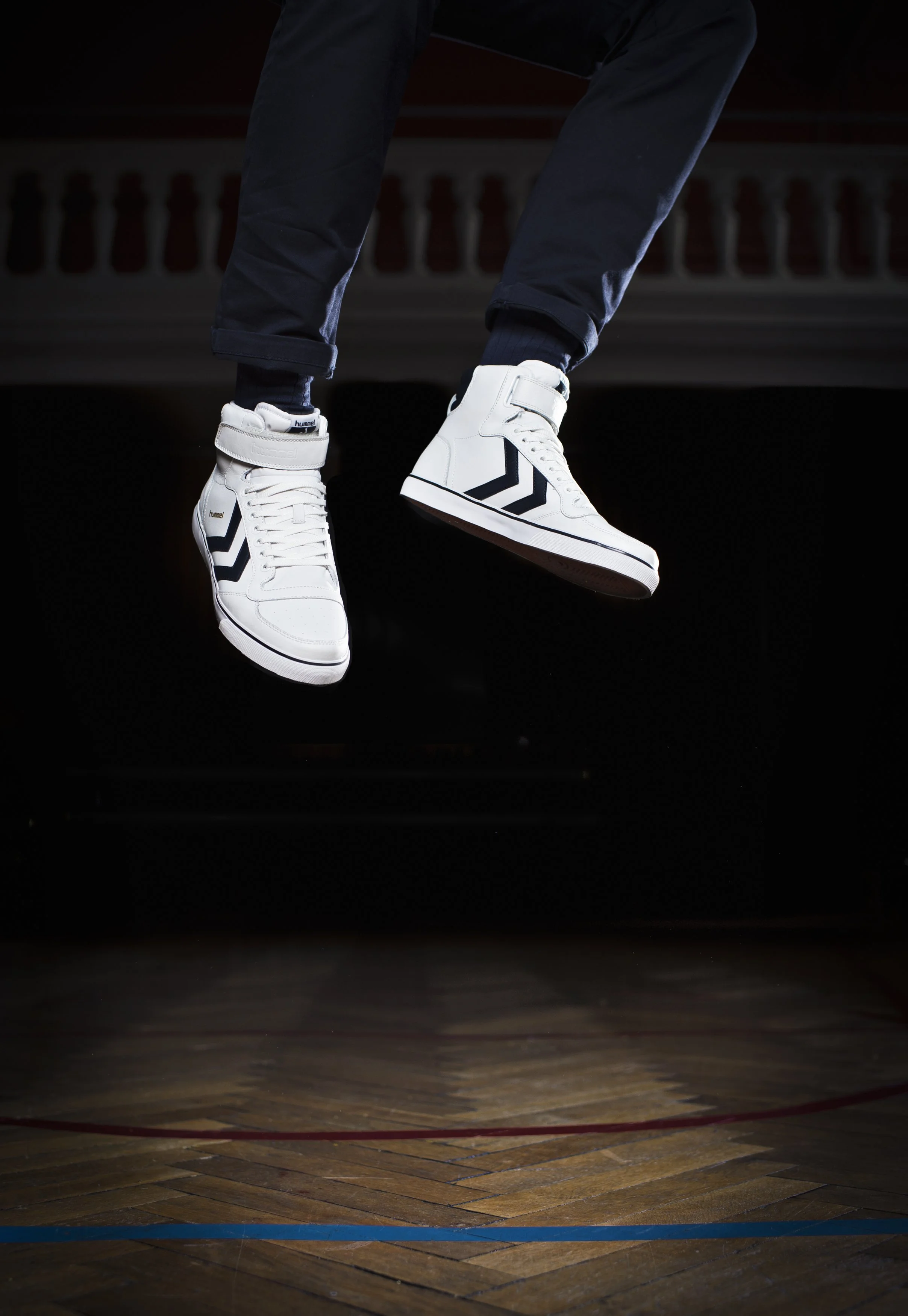 Chaussures de danse blanche suspendues au-dessus d'un parquet en bois, dans une pièce sombre avec lumière ciblée.