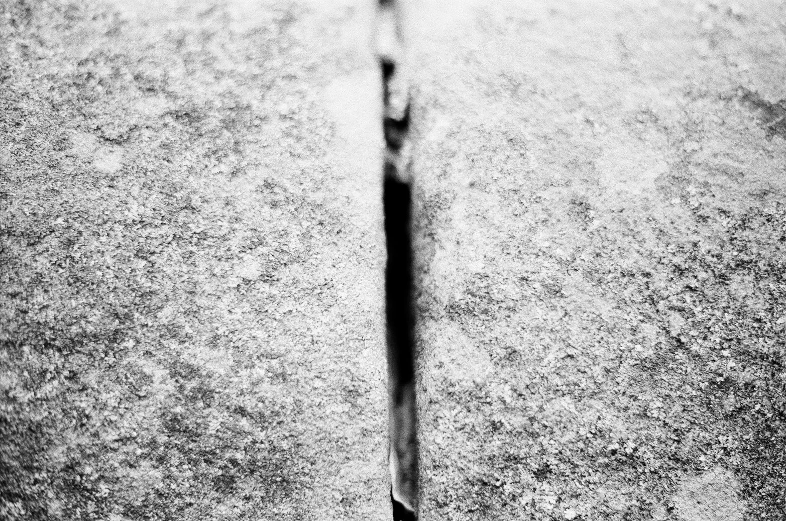 Close-up black and white photo of a cracked concrete wall with a narrow, vertical crack in the center.