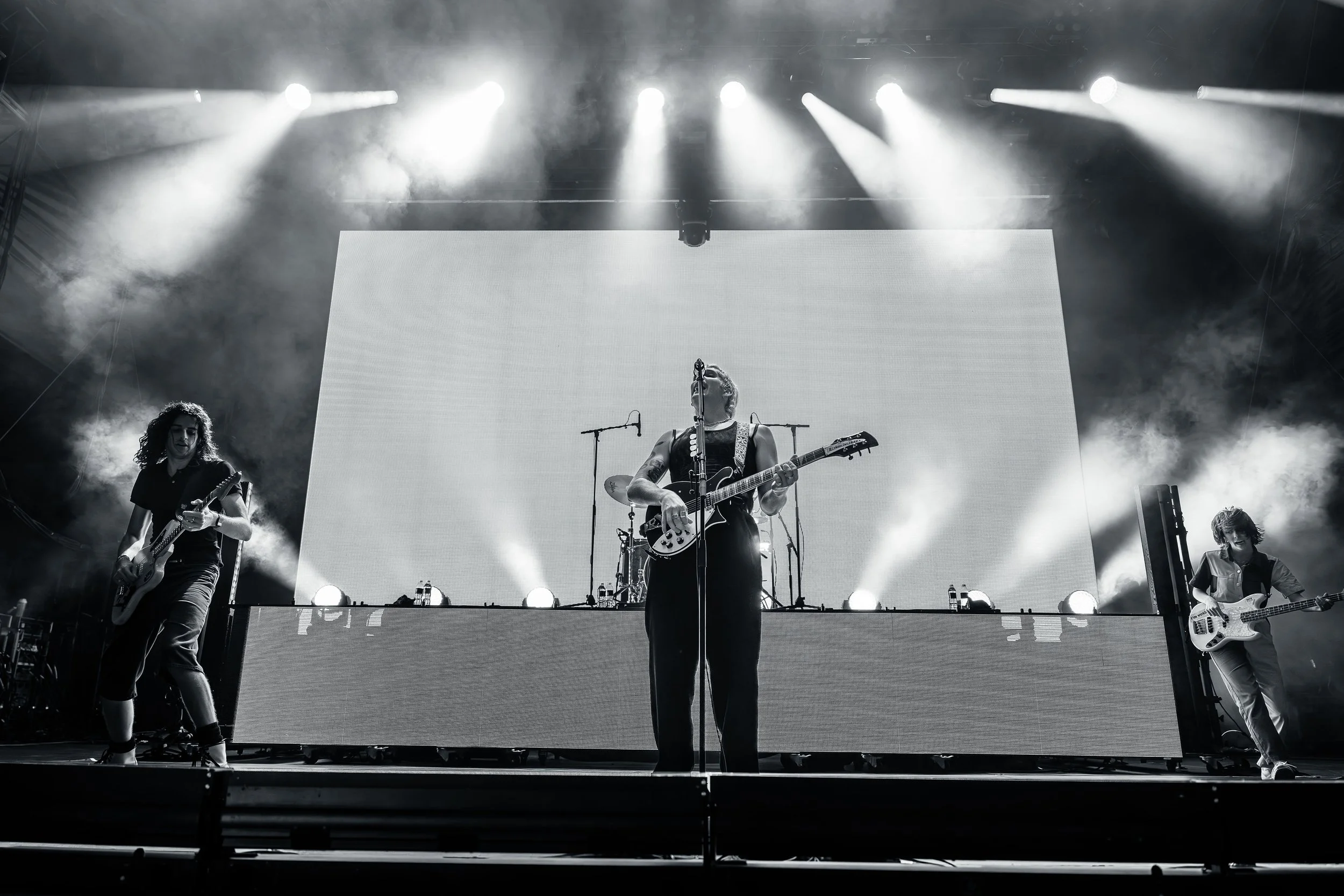 Black and white photo of a live band performance on stage with multiple musicians, guitars, microphones, and bright stage lighting.