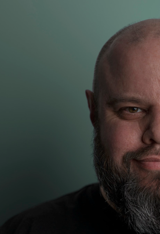 Close-up of a smiling man with a beard and bald head against a plain background.