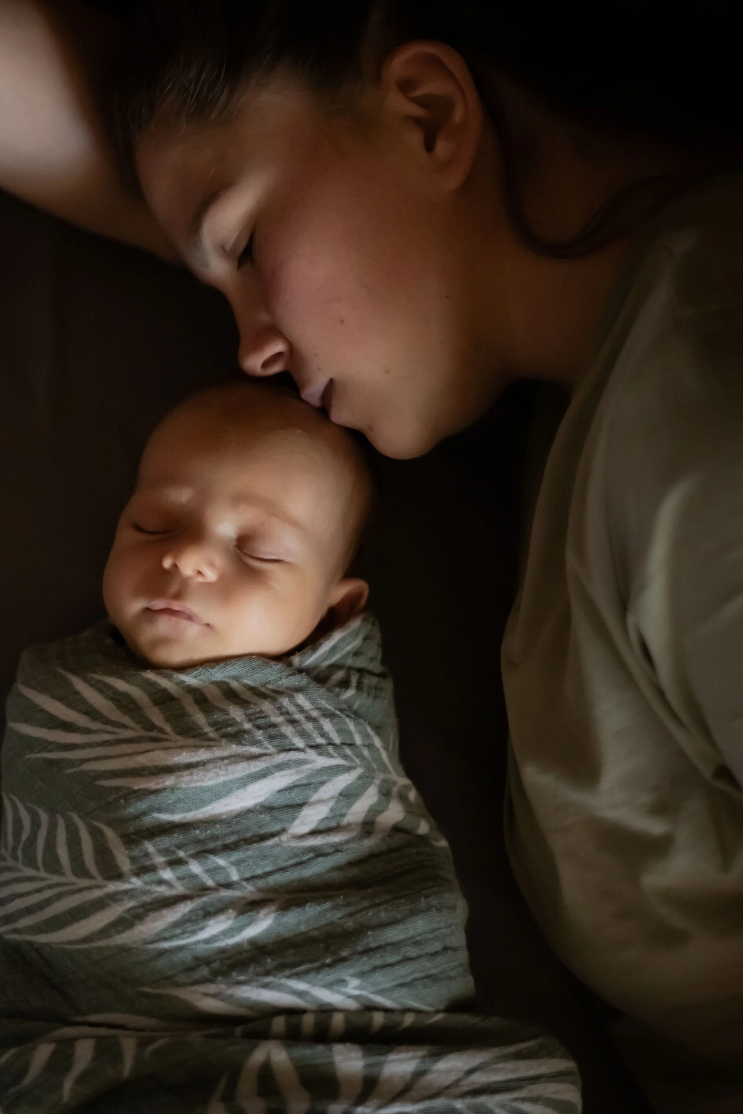 A woman and a young child sleep peacefully, their faces close together, on a dark surface.