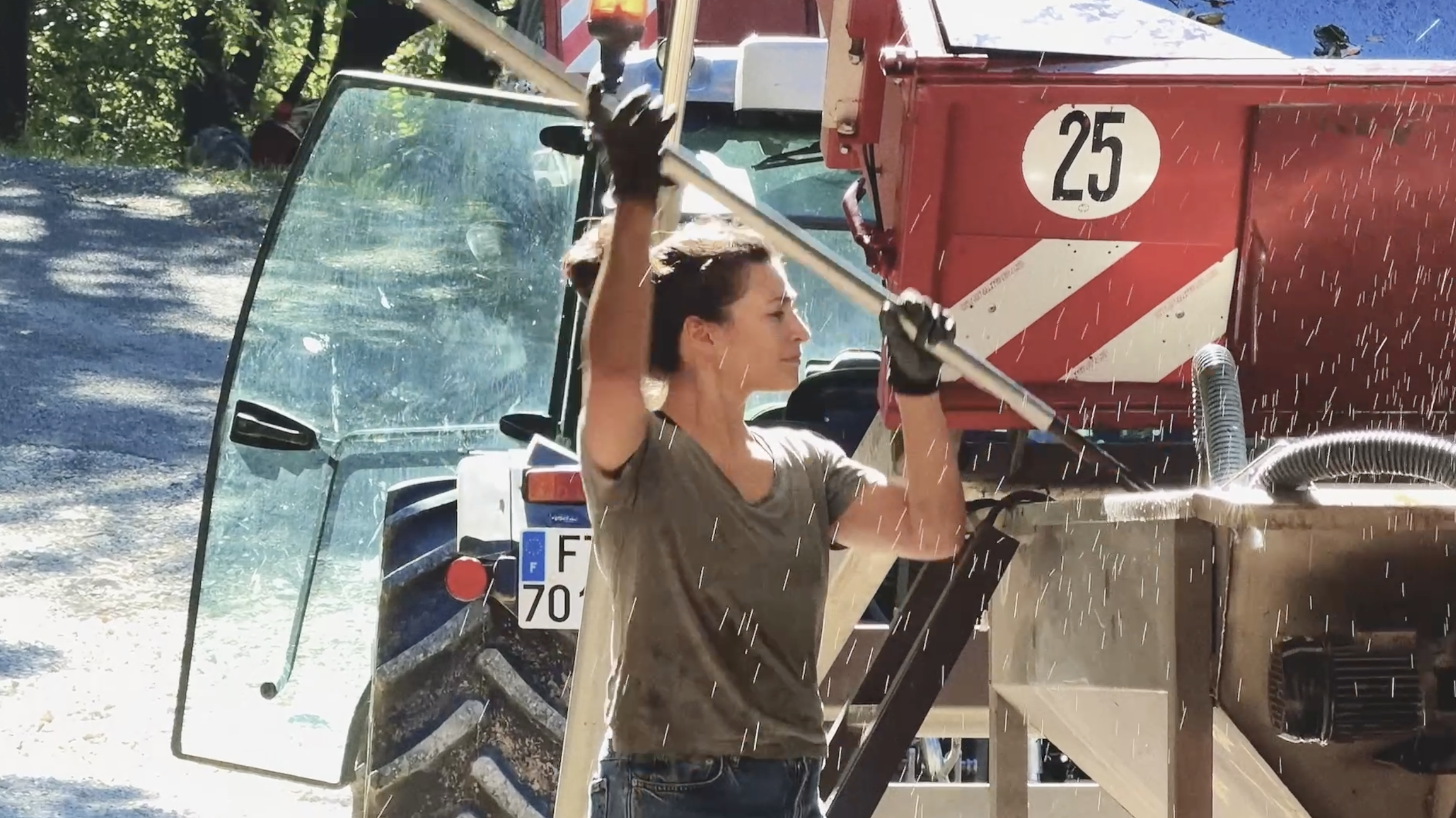 A woman operating a machine that sprays water, with trees and a vehicle in the background.
