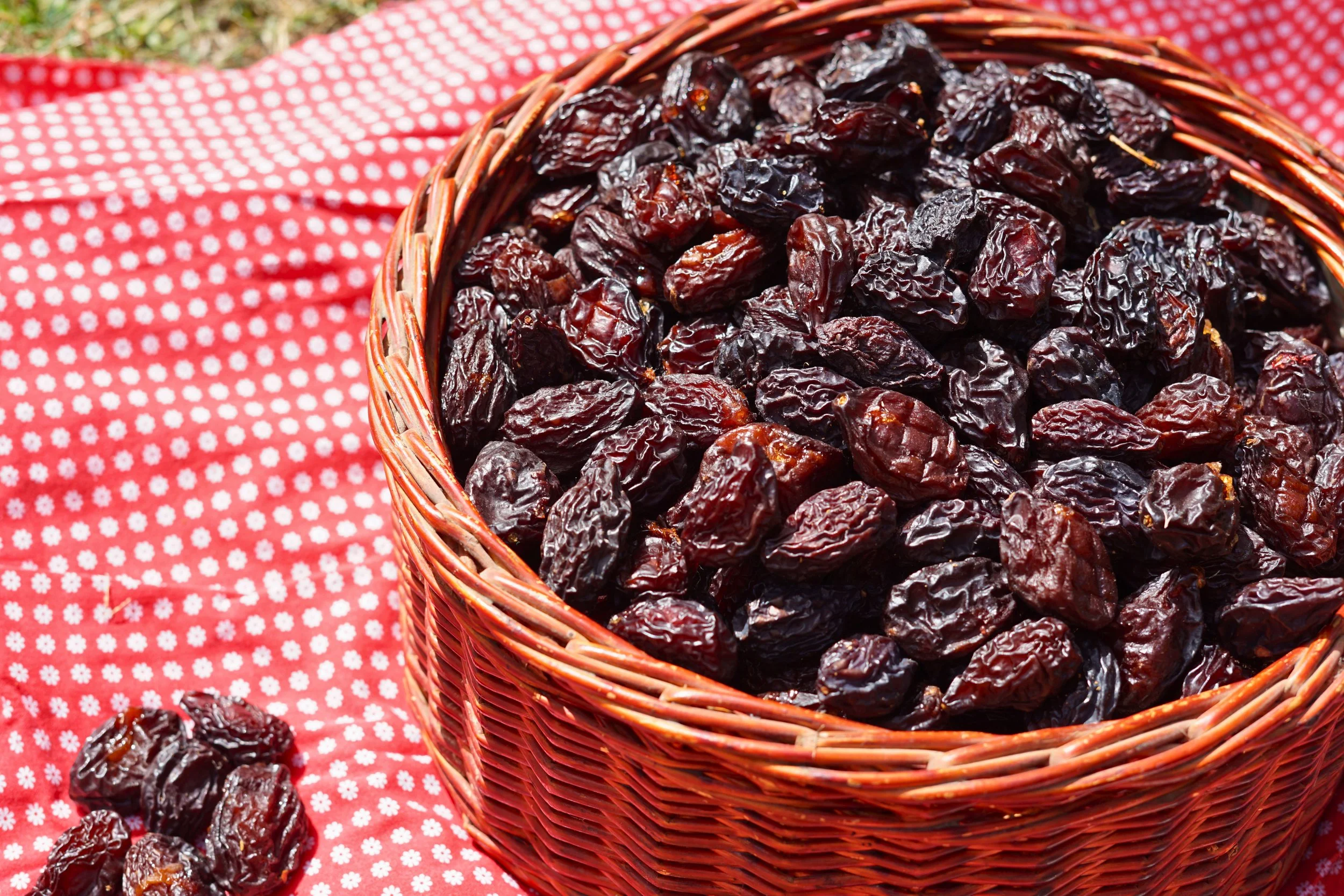 A wicker basket filled with dried dates placed on a red gingham cloth, with some dates scattered around.