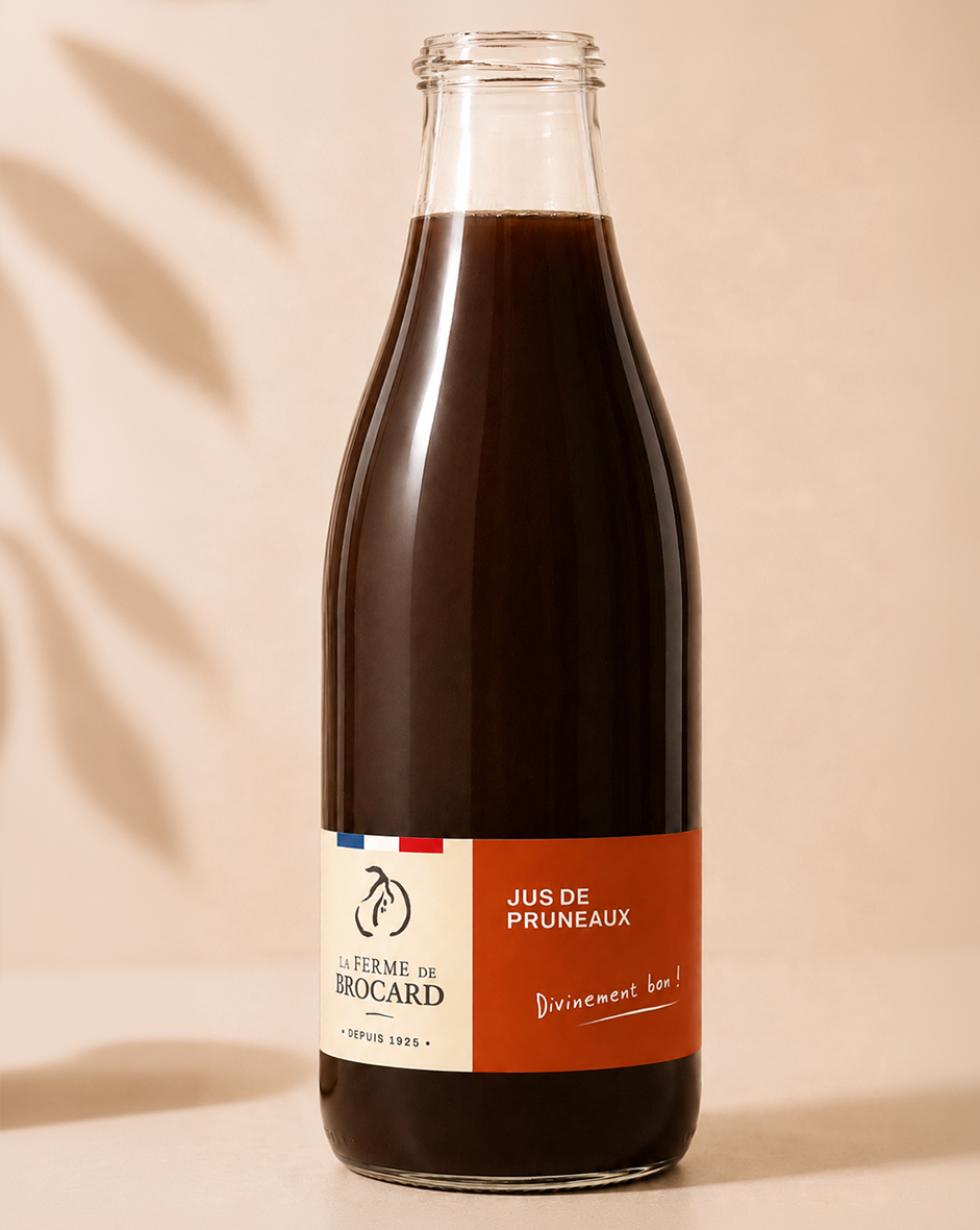 Bouteille en verre contenant du jus de pruneaux, avec une étiquette rouge et blanche, portant le nom 'Jus de Pruneaux' et le logo 'La Ferme de Brocard'.
