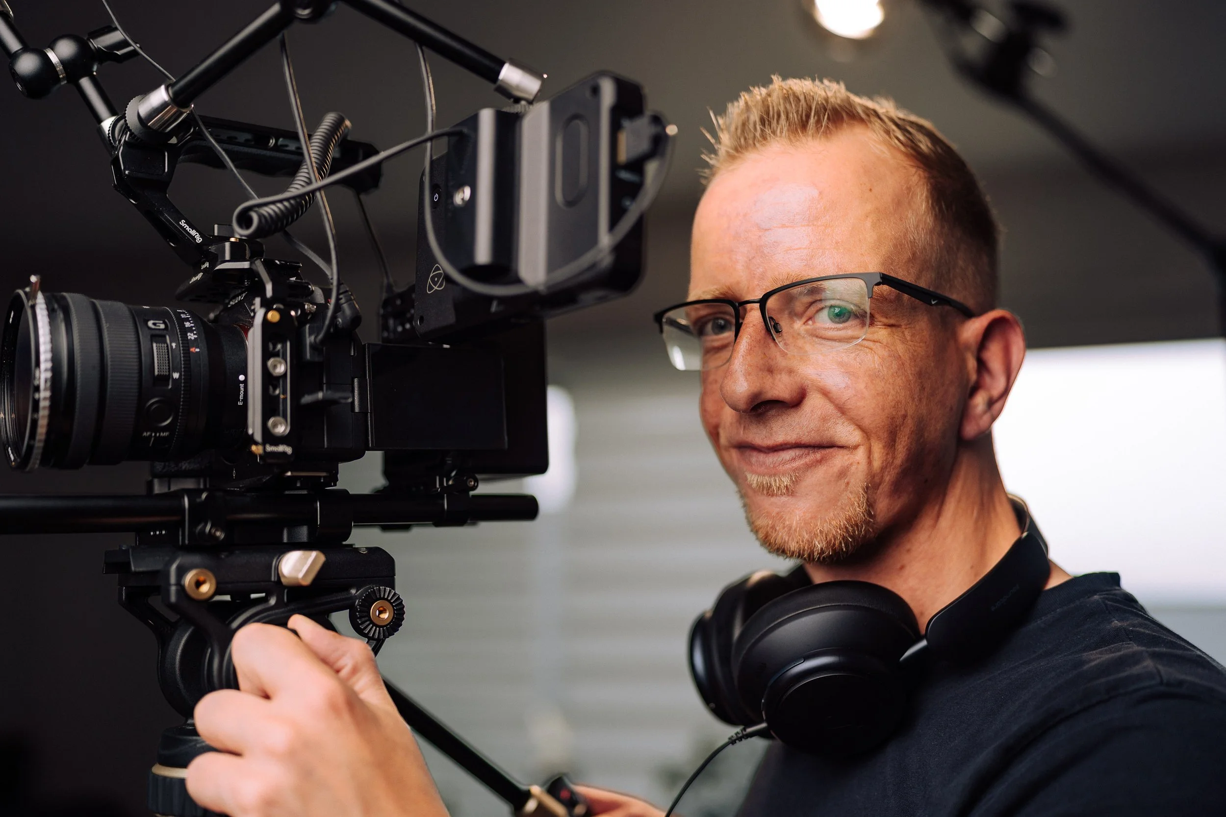 Ein Mann mit Brille, der eine professionelle Kamera auf einem Stativ bedient.