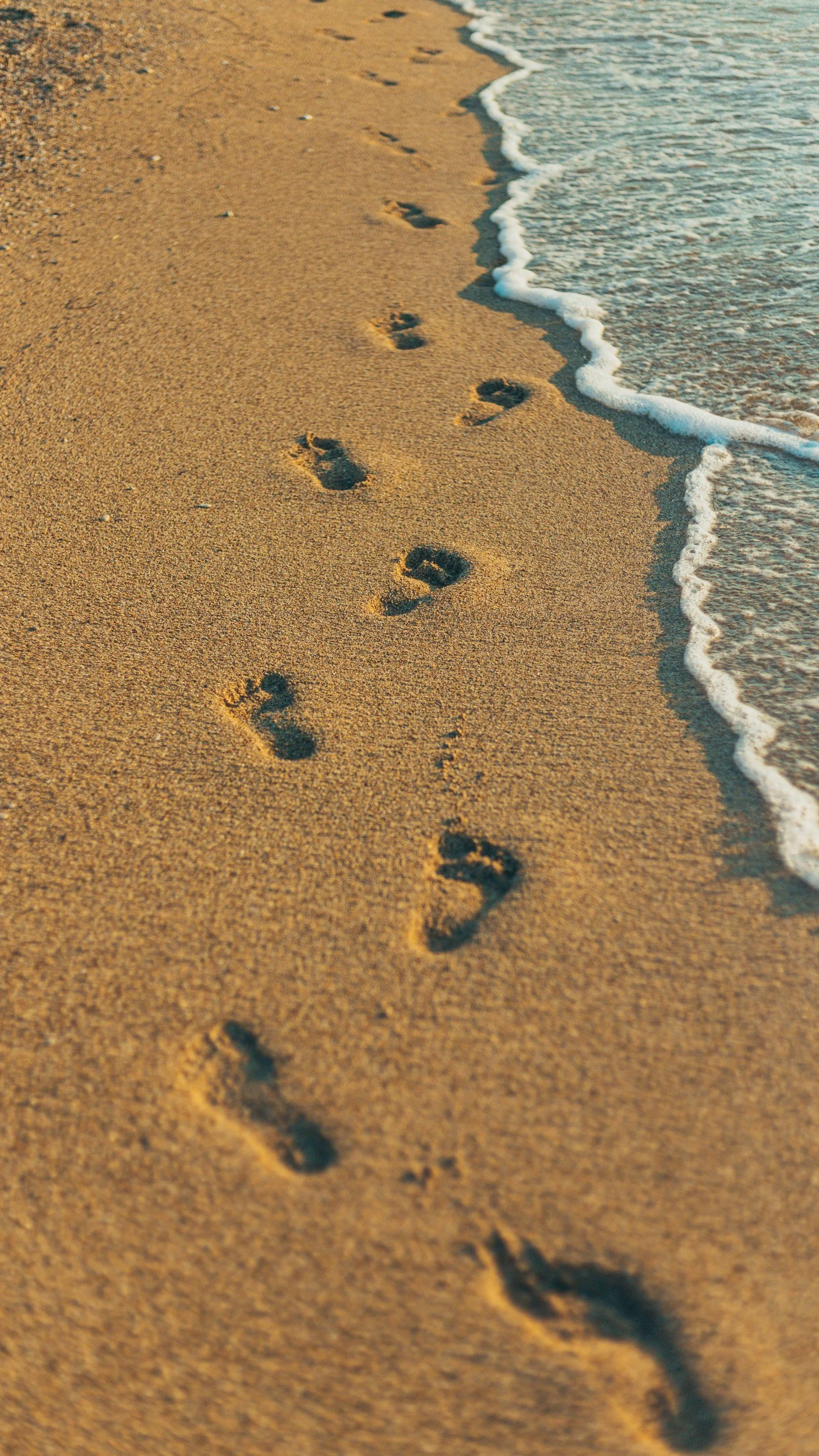 Footprints in sand along the shoreline, with gentle waves washing up on the beach.