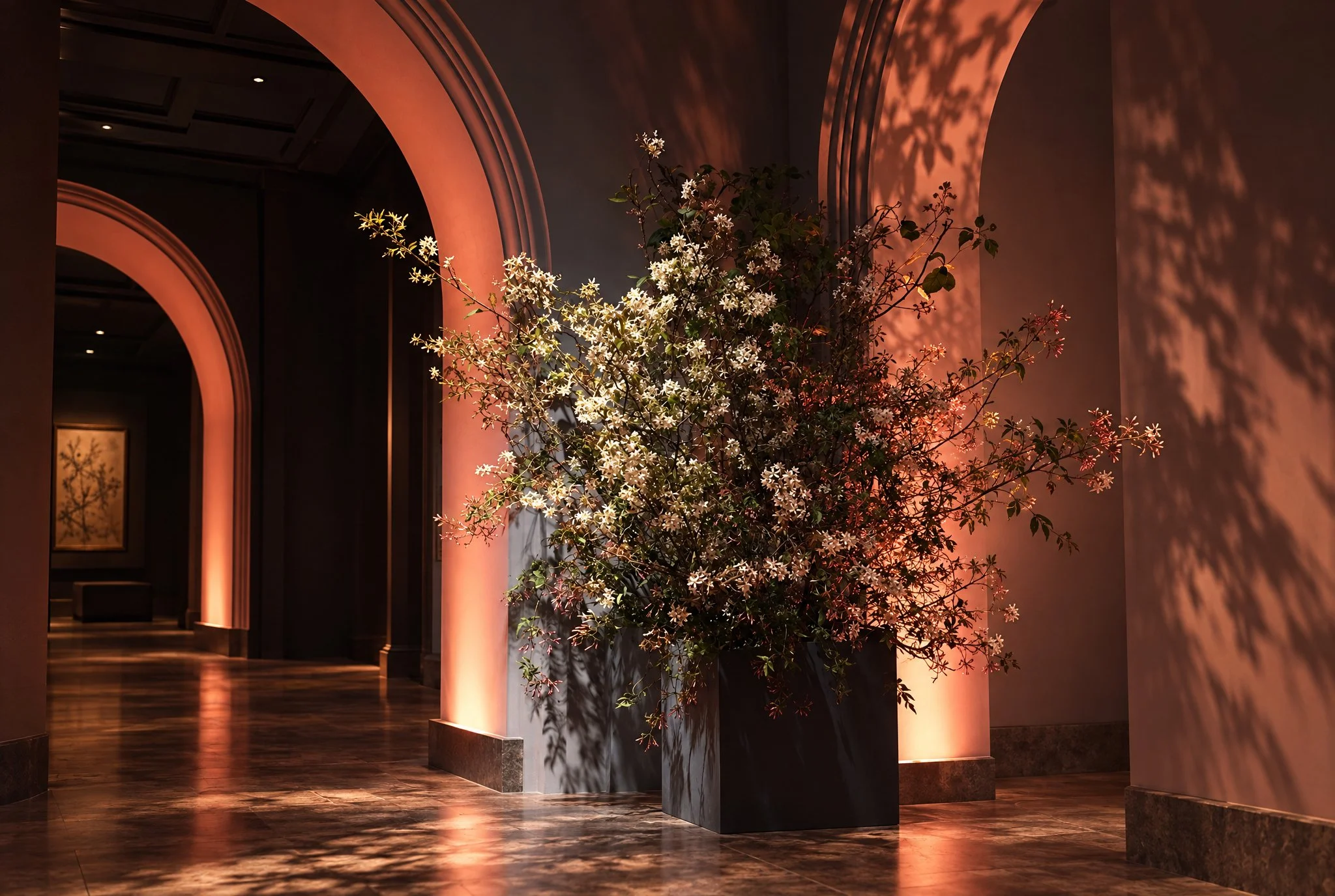 Indoor space with arched doorways, a large flower arrangement in a tall vase, and soft warm lighting casting shadows on the wall.
