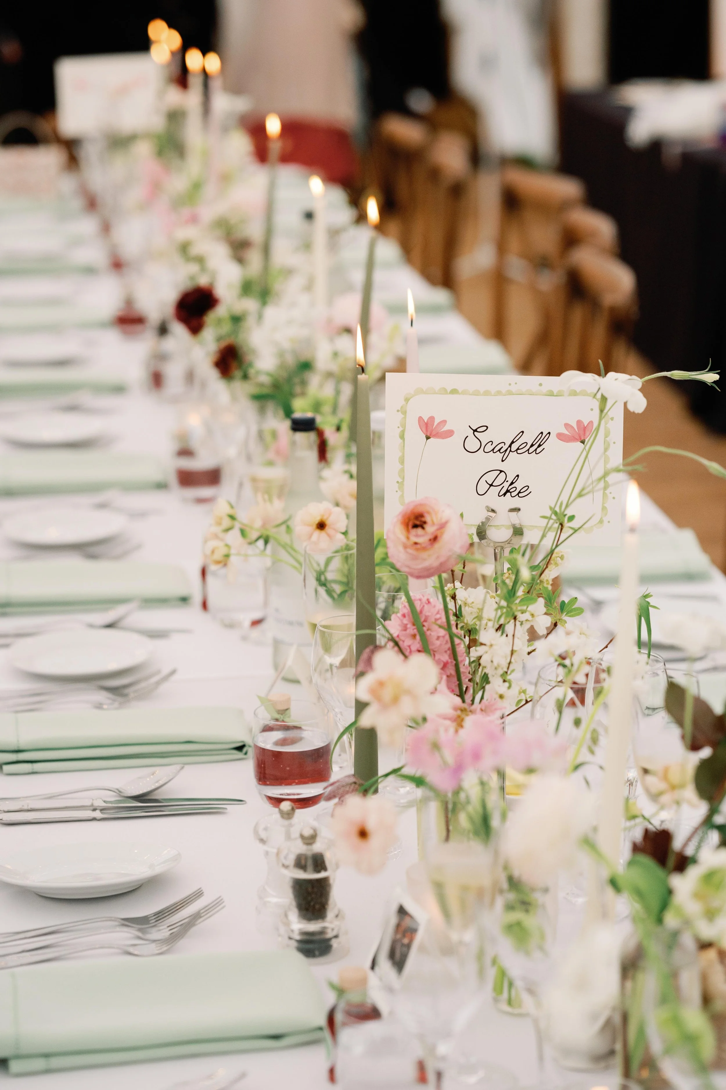 Elegant banquet table decorated with pink and white flowers, candles, and place settings, with a sign reading 'Scafell Pike.'