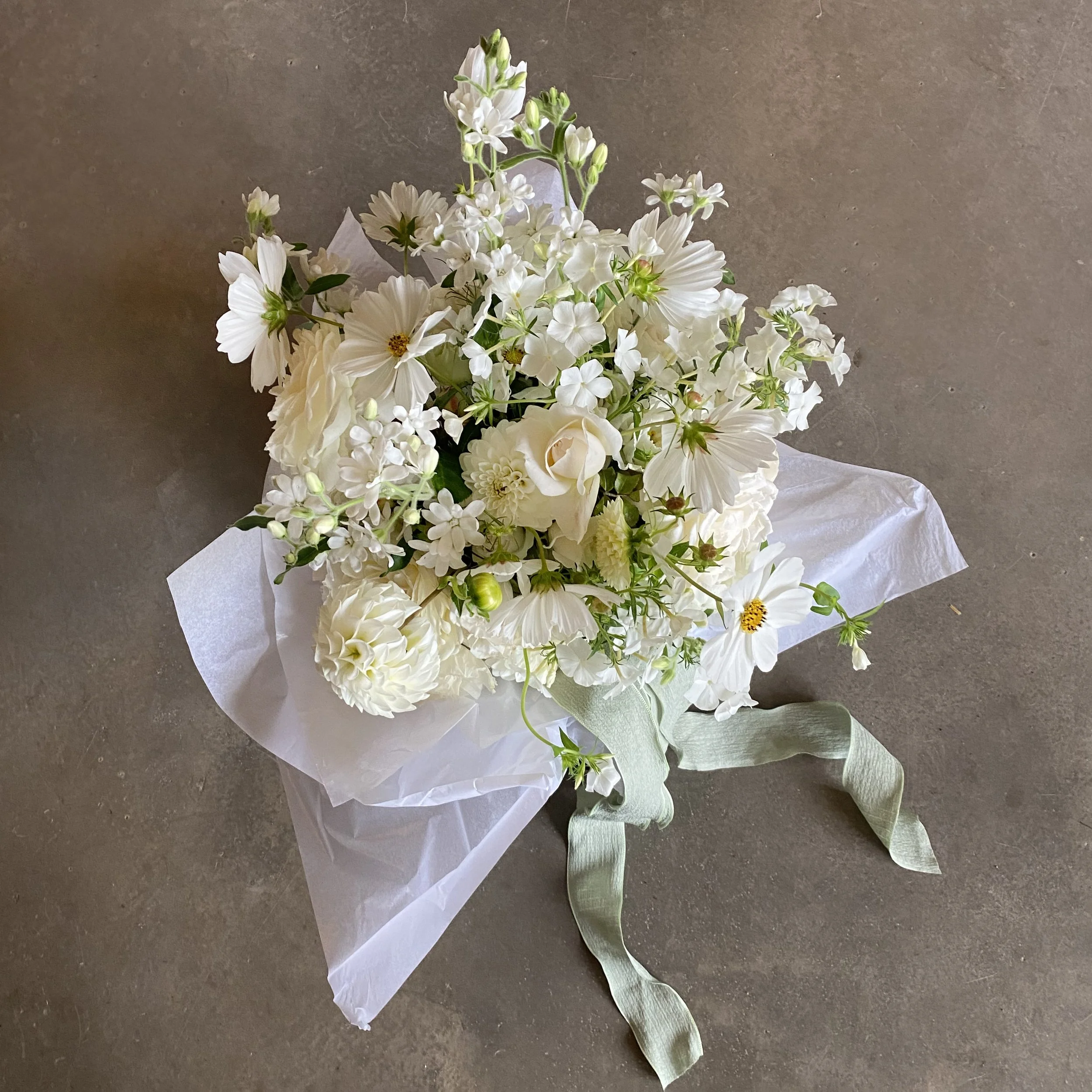 A bouquet of white flowers wrapped in tissue paper on a gray surface.