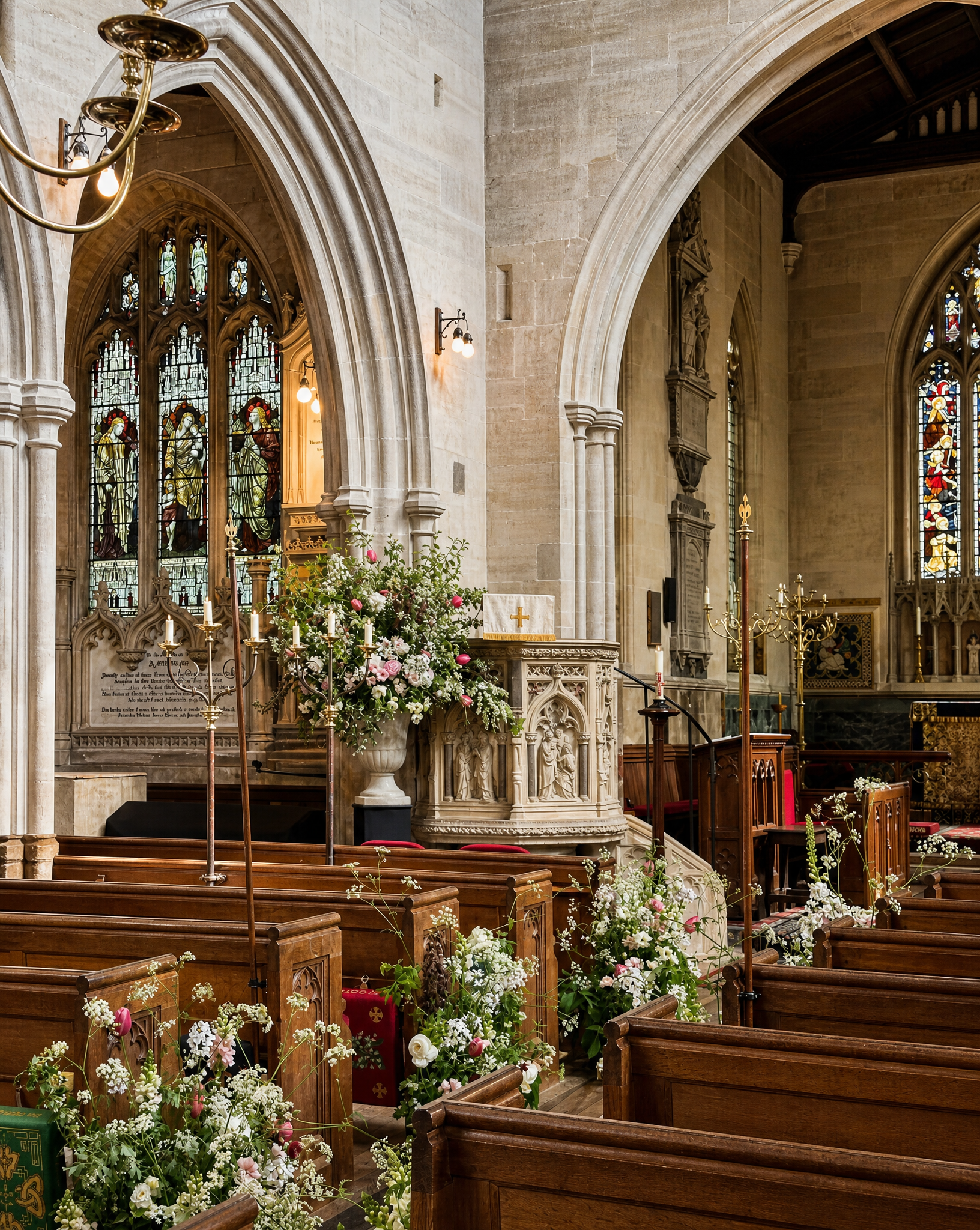 Interior view of a church with stained glass windows, wooden pews, floral arrangements, and religious decorations.