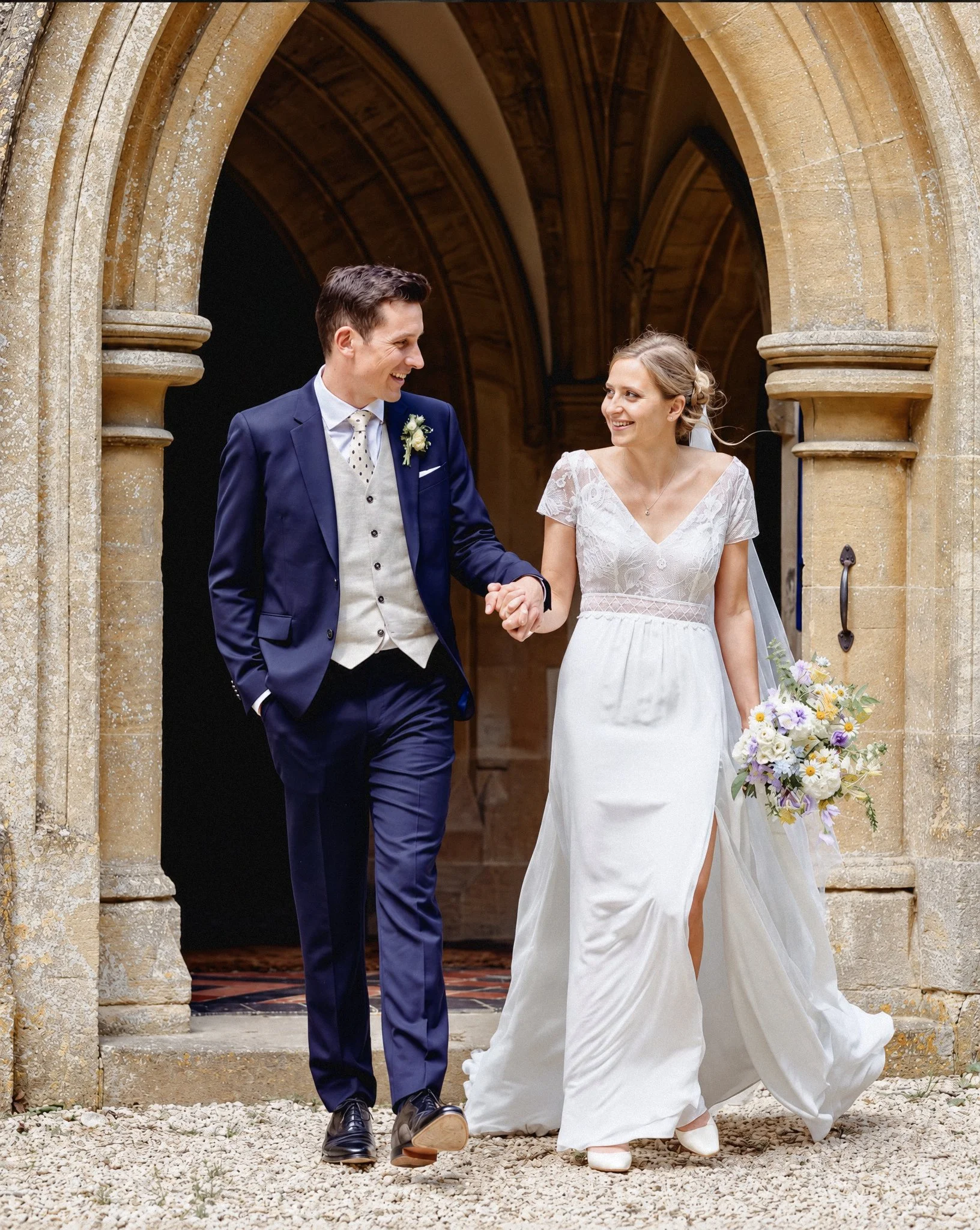 A smiling groom and bride holding hands and walking out of a church.
