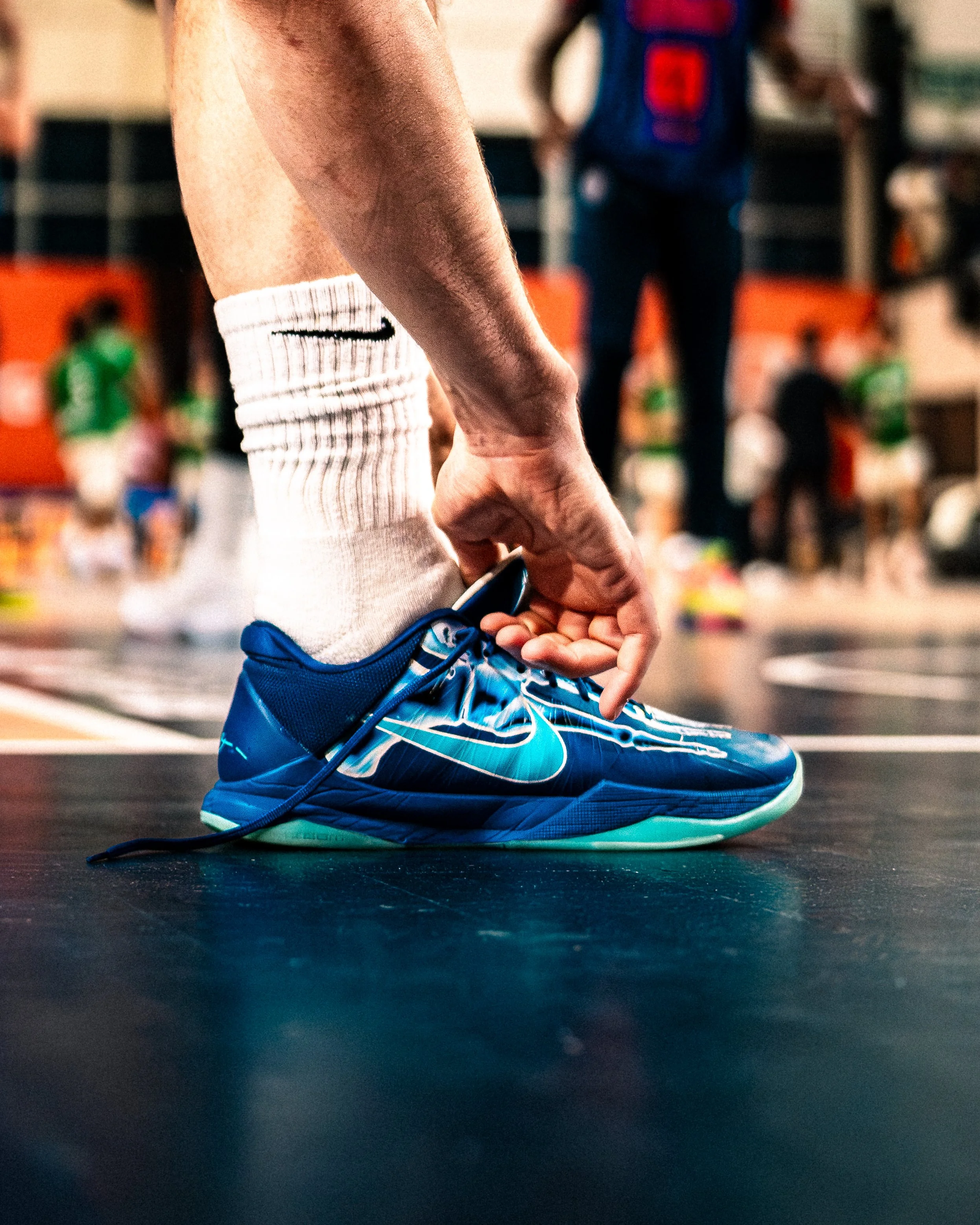 Un athlète en train de s'attacher la chaussure de course, portant des chaussettes blanches, un short bleu, et des chaussures de sport bleues, dans une salle d'entraînement ou un gymnase.