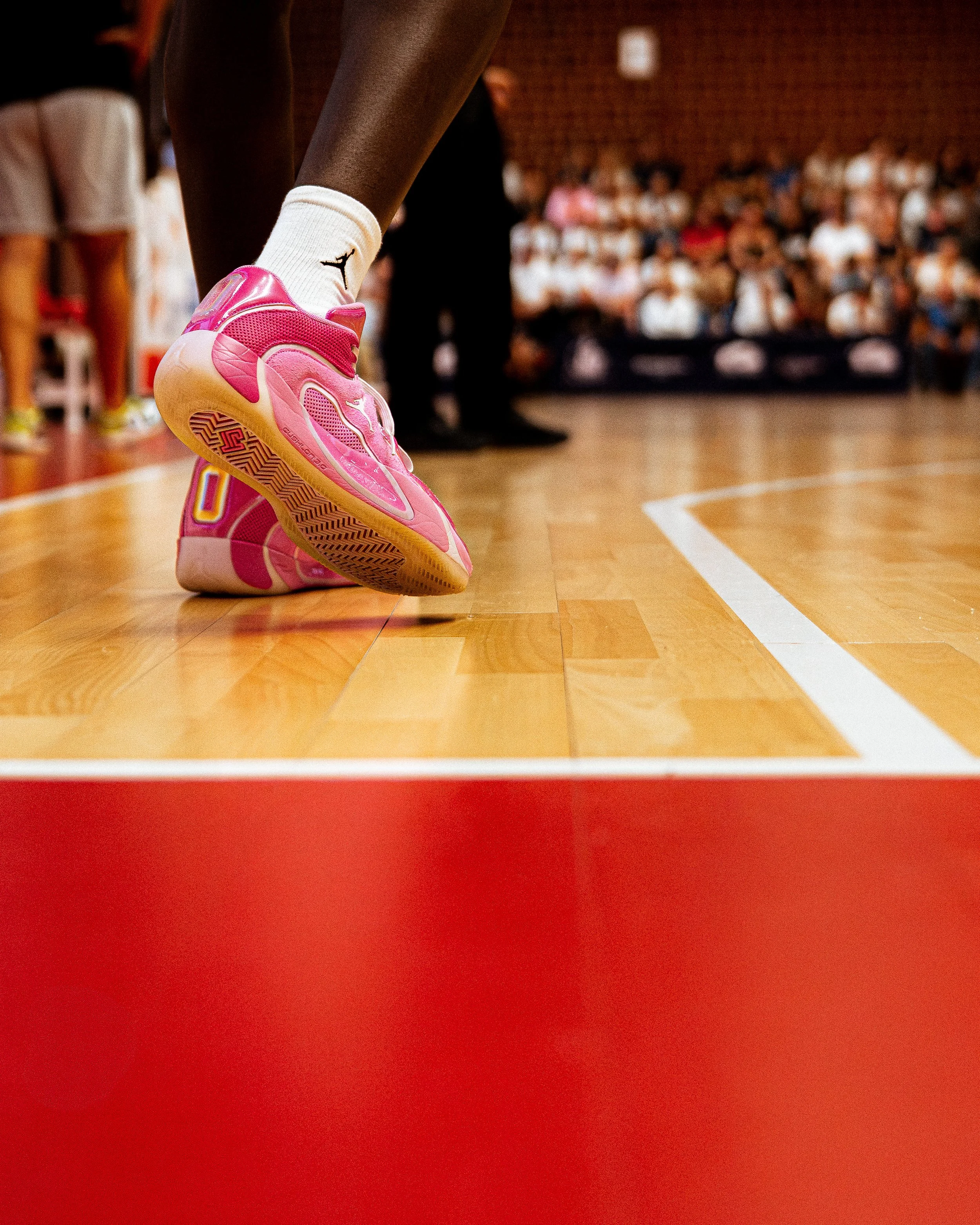 Un joueur de basket en train de se préparer à faire un lancer franc sur un terrain en intérieur, un public assis en arrière-plan.