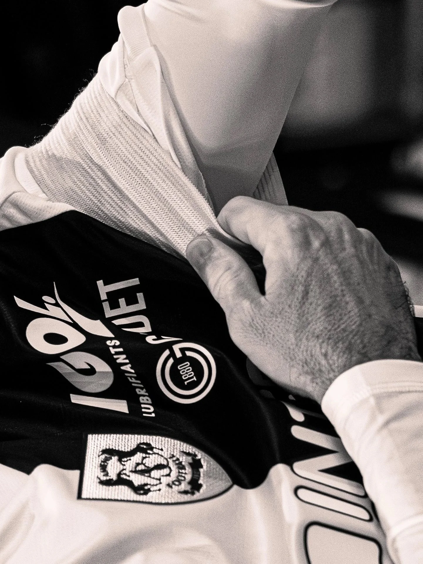 Une main portant un gant blanc manipulant un vêtement noir avec un logo, vêtements de sport, photographie en noir et blanc.