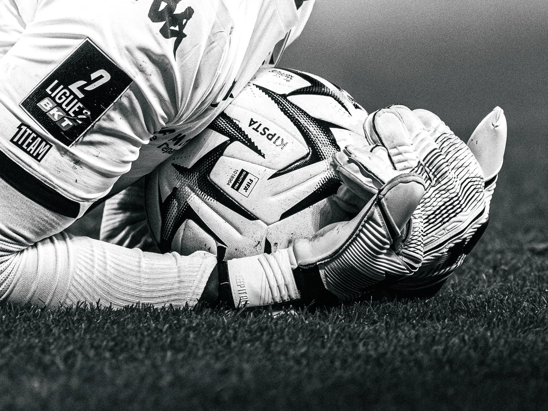 Photo en noir et blanc d’un joueur de football en position de défense, portant un maillot à manches longues et un gant, sur un terrain en herbe.