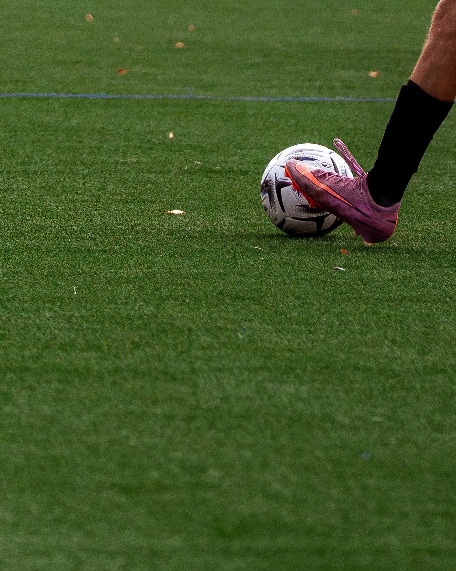 Un joueur de football portant une chaussure violette est sur un terrain d'herbe verte, posant son pied sur un ballon de football.