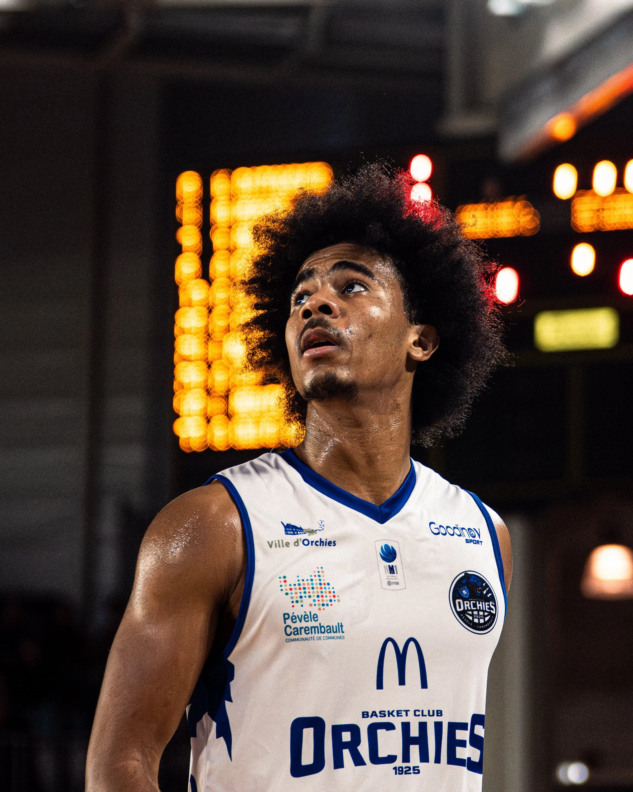 Jeune joueur de basket-ball portant un maillot de l'équipe Orcines, en pleine action lors d'un match ou entraînement, avec un fond de lumières floues. 