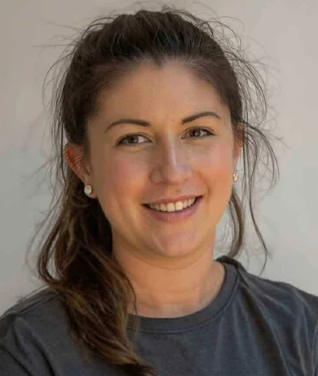 A woman with dark hair in a ponytail smiling at the camera, wearing a dark shirt and pearl earrings.