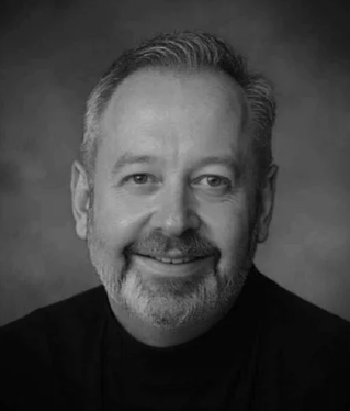 Black and white portrait of a man with short, styled hair, a beard, and a smile.