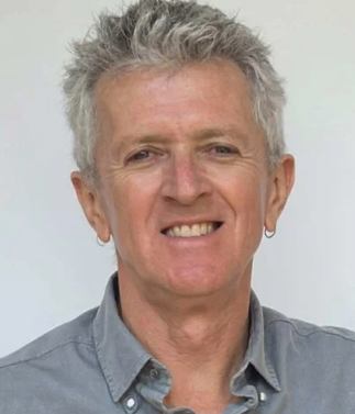 Portrait of a smiling middle-aged man with gray hair, wearing a gray collared shirt.