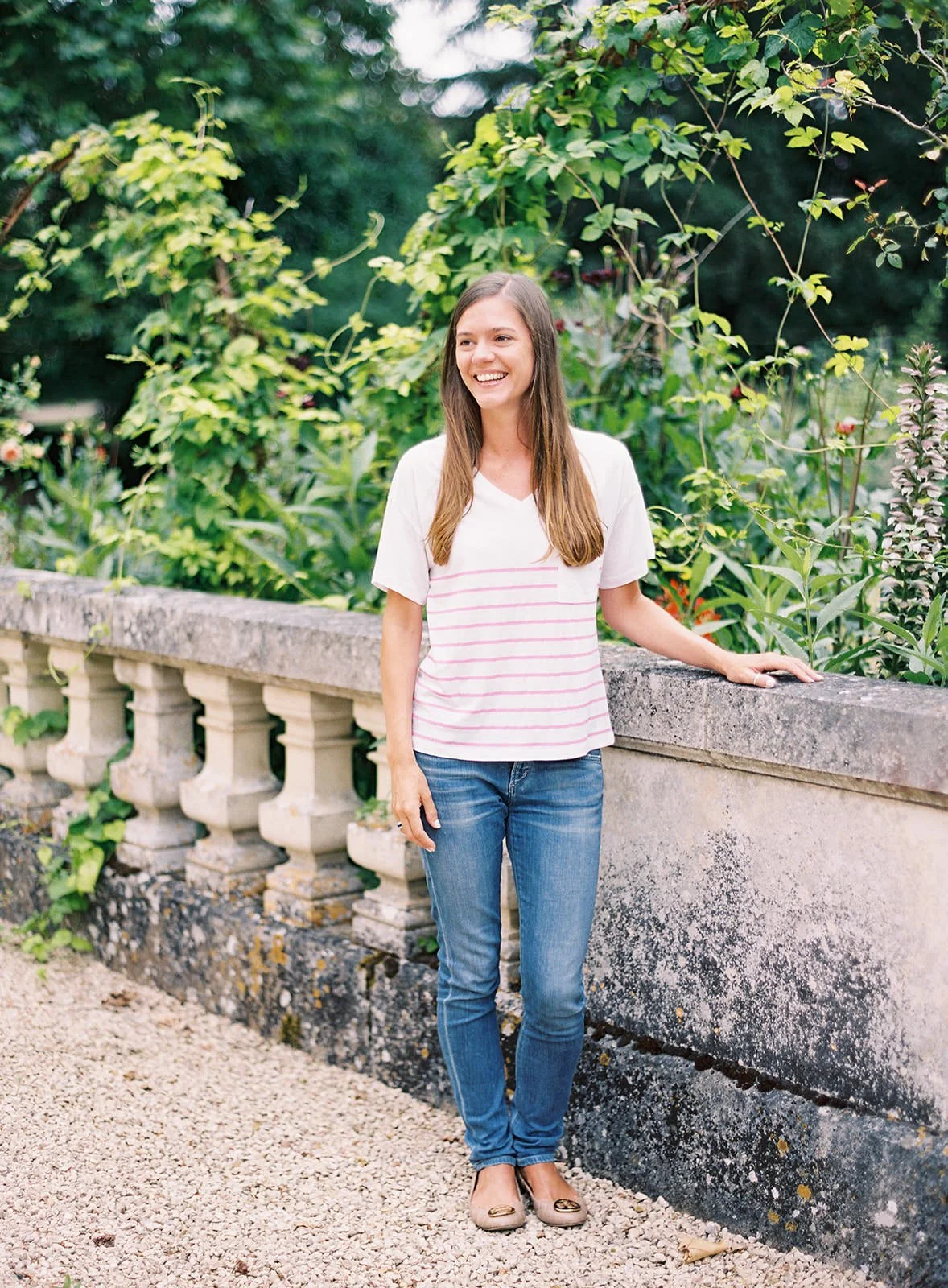 Lucy Davenport standing next to a stone railing, smiling, surrounded by lush greenery and plants.
