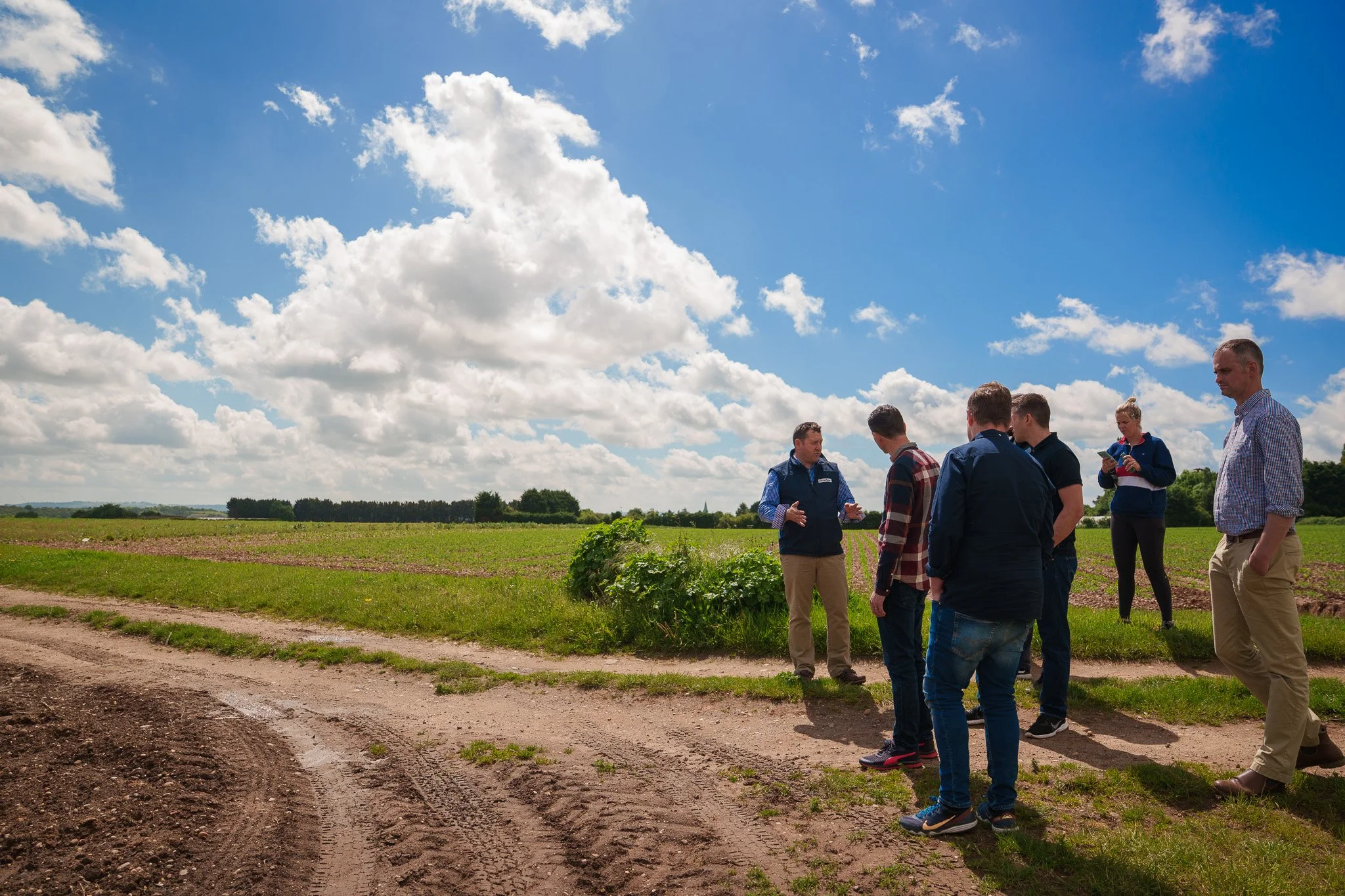Group of people standing in a field under a partly cloudy sky, engaged in conversation.