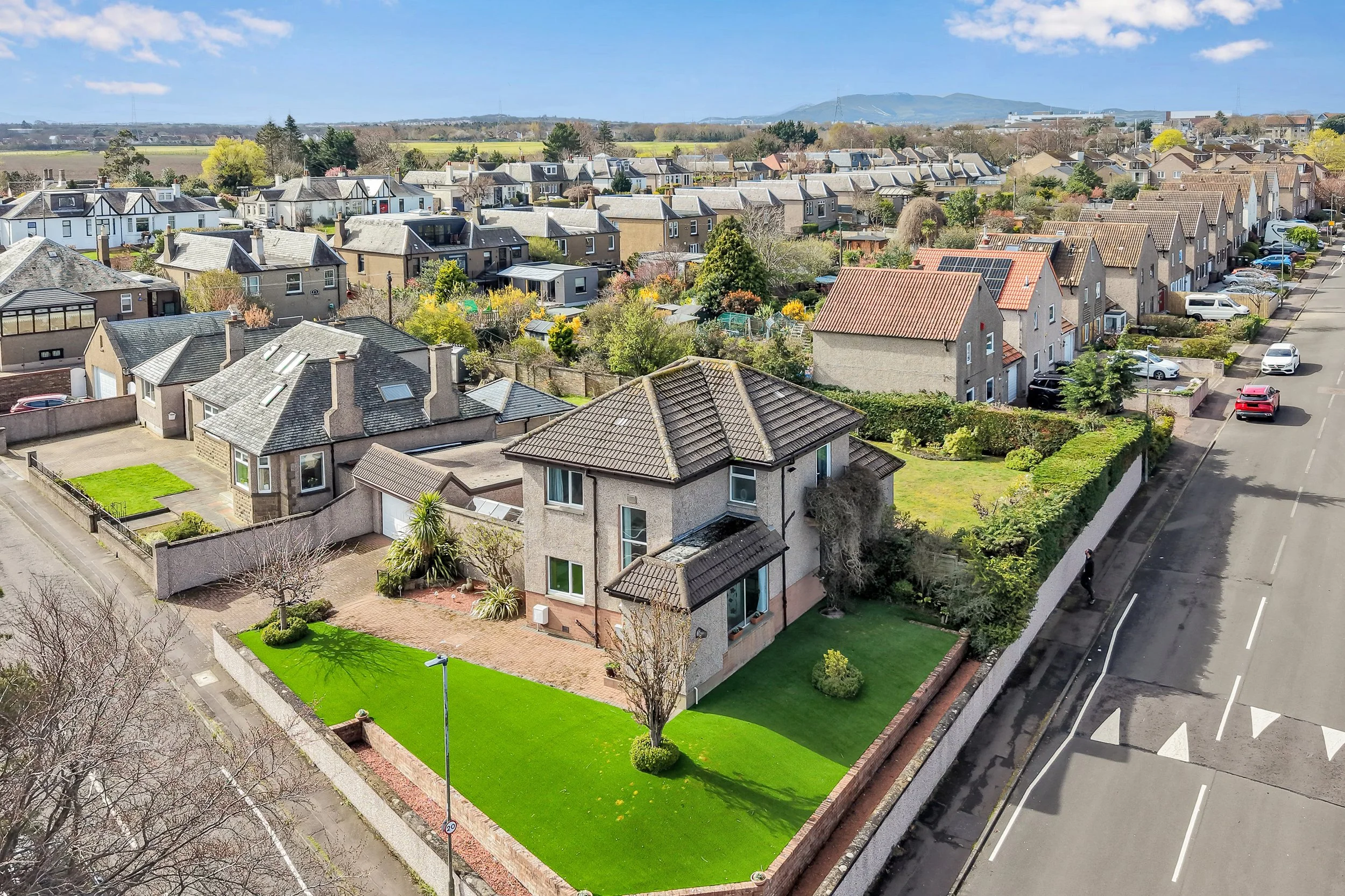 Aerial view of a suburban neighborhood with houses, trees, and a street with parked cars on a sunny day.
