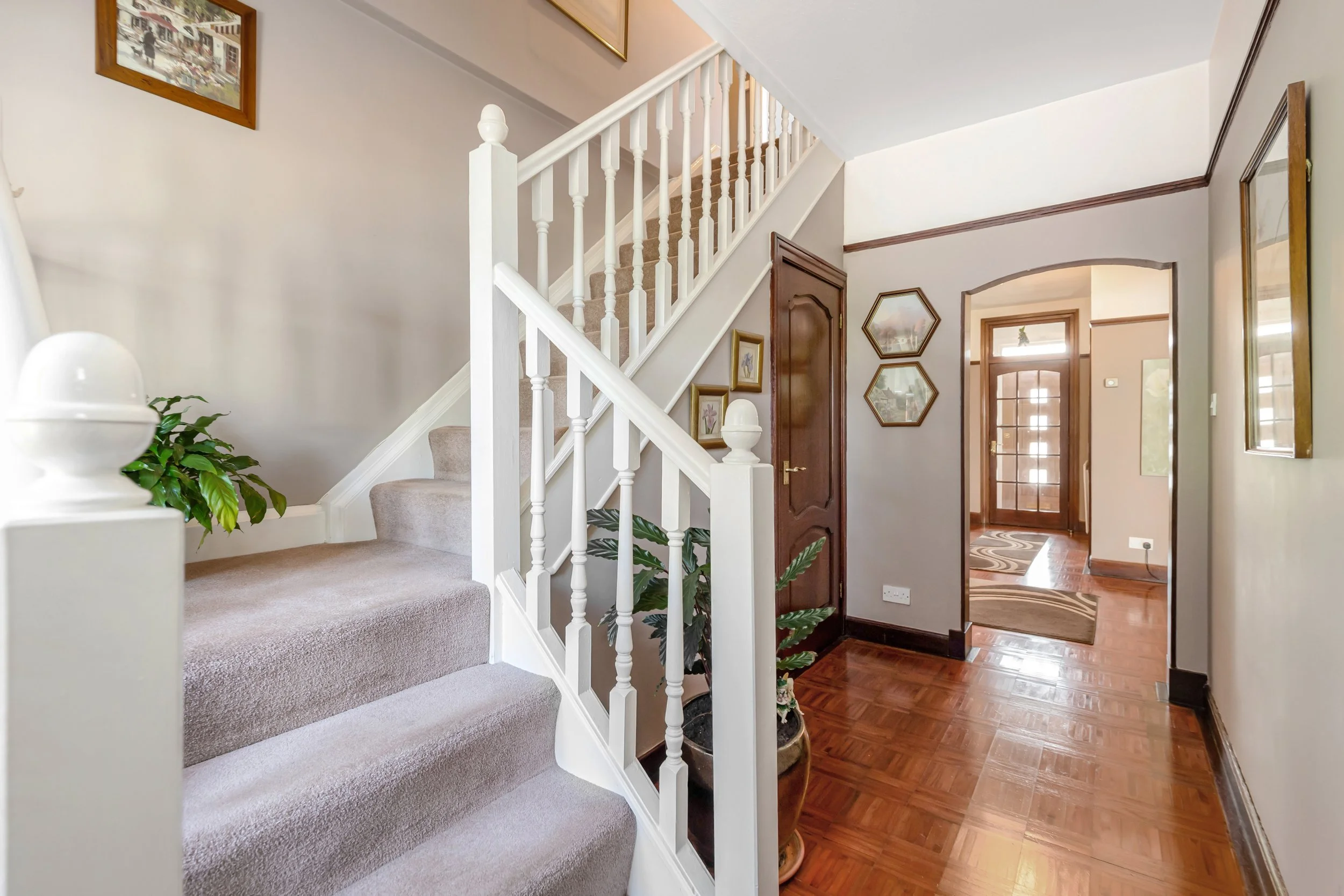Interior view of a house entryway with stairs, a wooden door, framed pictures, and hardwood flooring.
