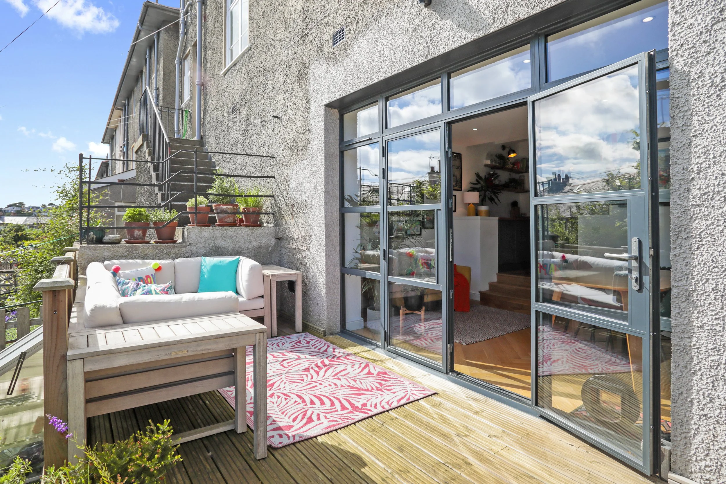 Balcony with outdoor seating area, potted plants, and glass sliding door leading inside an apartment.