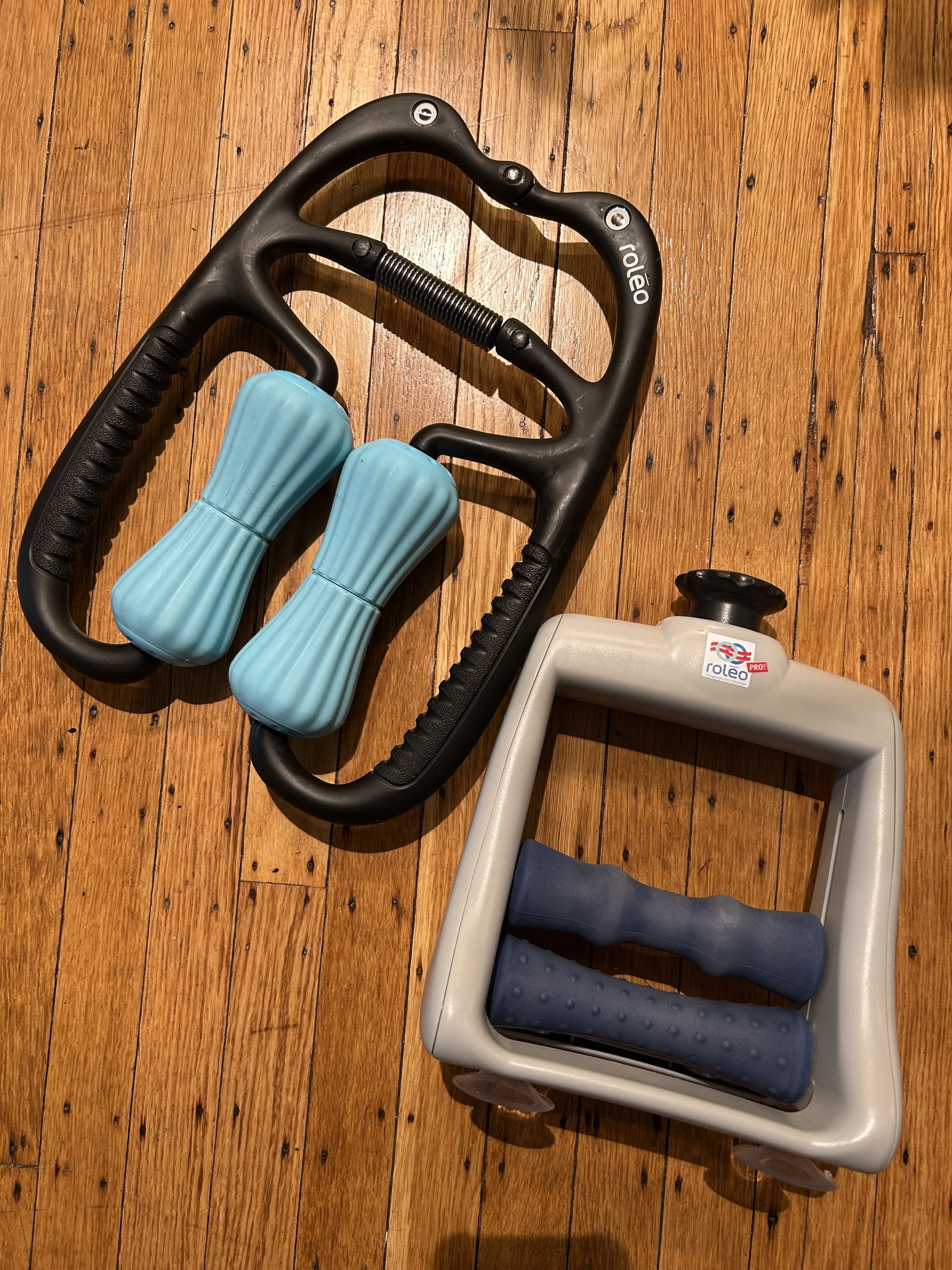 A black and gray hand exerciser with blue silicone grips and a blue plastic frame on a wooden floor.