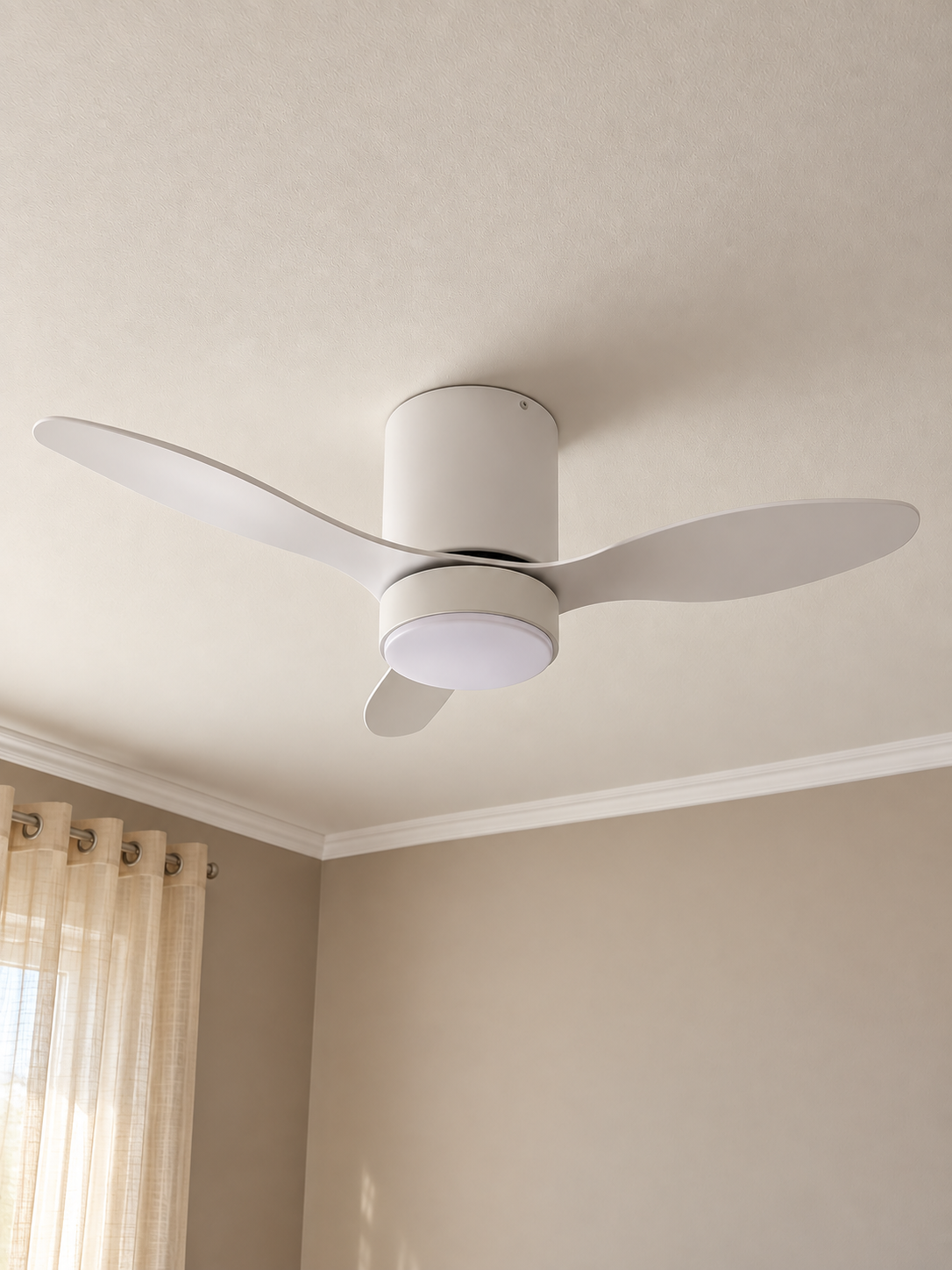 Ventilateur de plafond blanc avec trois pales, installé au plafond d'une pièce avec murs beige, moulures blanches et rideaux beige.