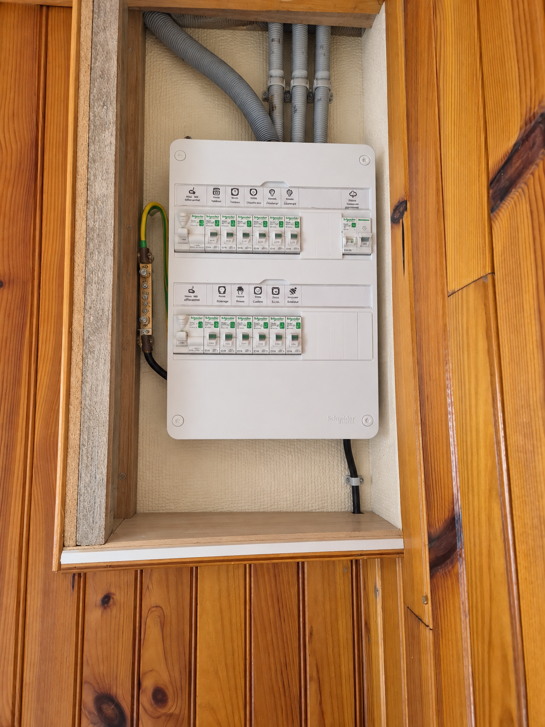 Une boîte à disjoncteurs électrique encastrée dans un mur en bois, avec plusieurs interrupteurs et câbles électriques suspendus.