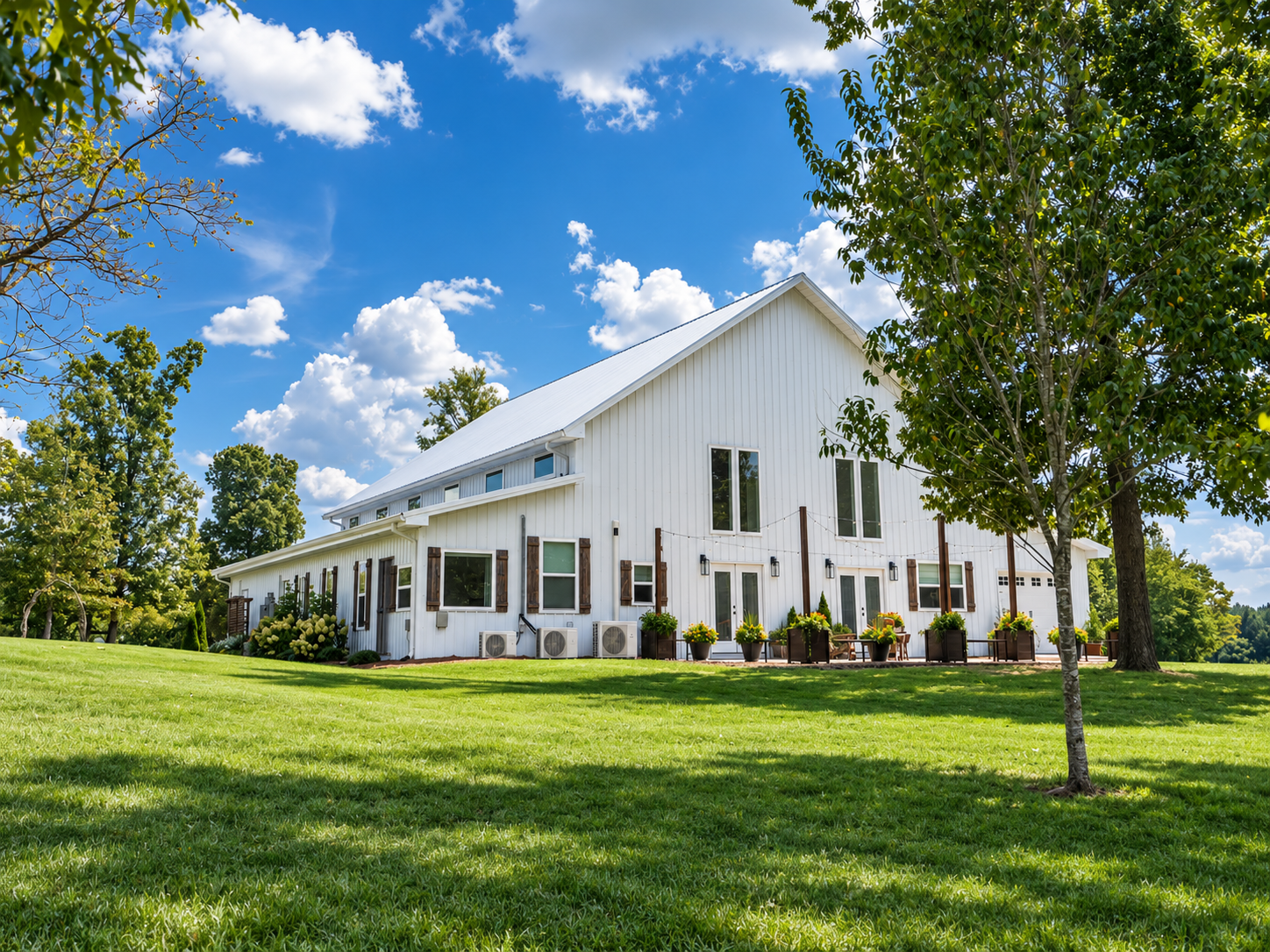 A white modern house with a sloped roof, surrounded by lush green grass and trees, under a partly cloudy blue sky.