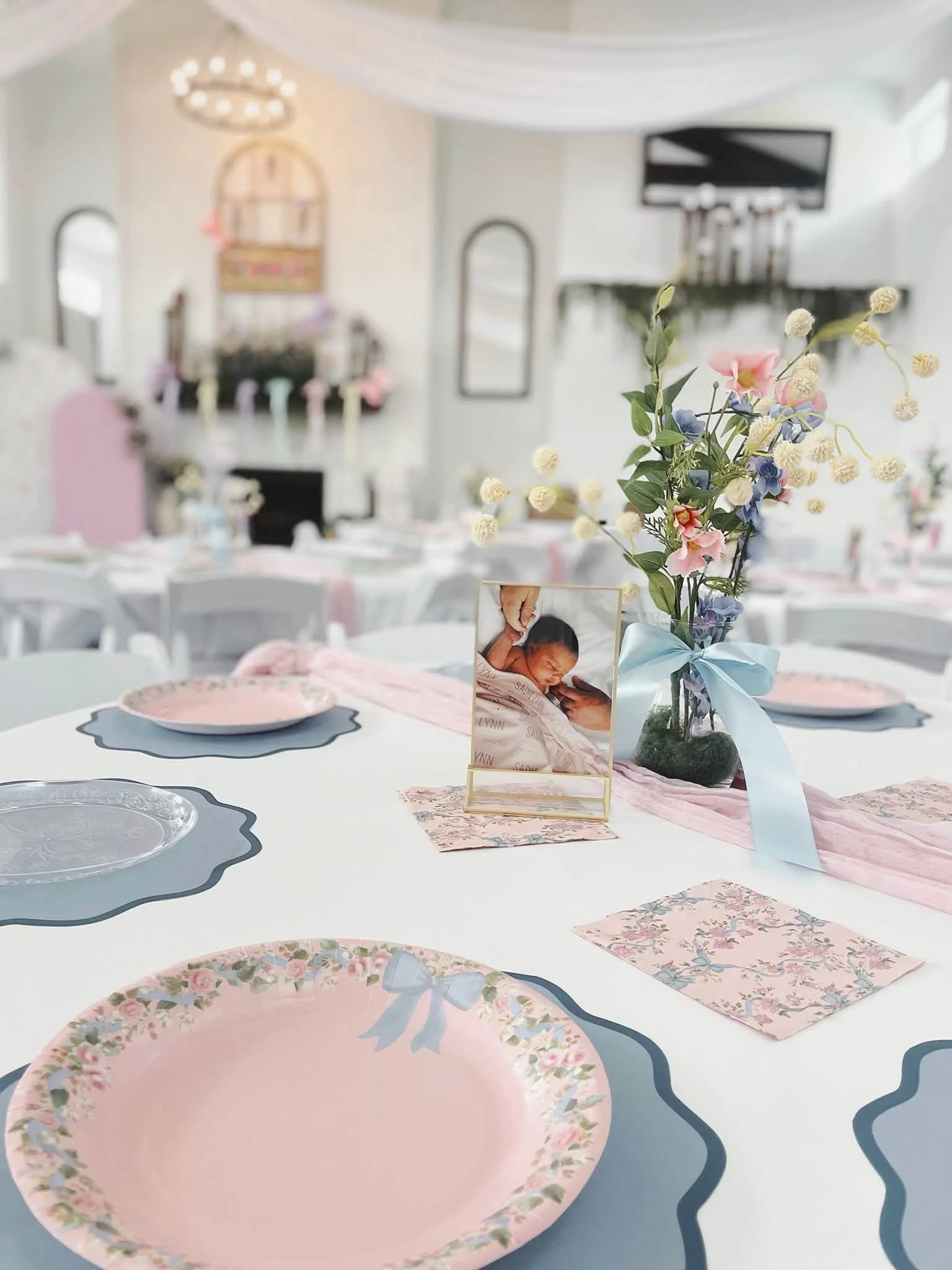 A decorated event table with pastel pink, blue, and floral themed tableware and centerpiece.