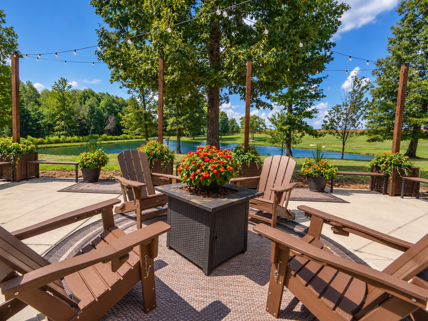 Outdoor patio with Adirondack chairs and potted flowers overlooking a lake and green trees under a blue sky.