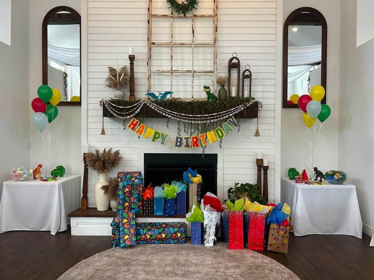 A decorated living room with a fireplace, birthday banner, balloons, and wrapped gifts for a birthday celebration.