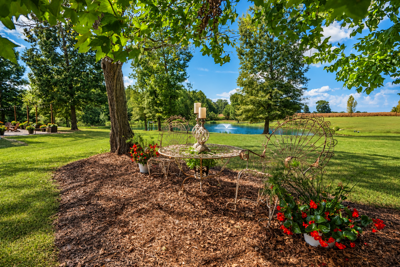 Wrought iron outdoor table and chairs with candles, potted plants, and a pond with fountain in a lush garden.