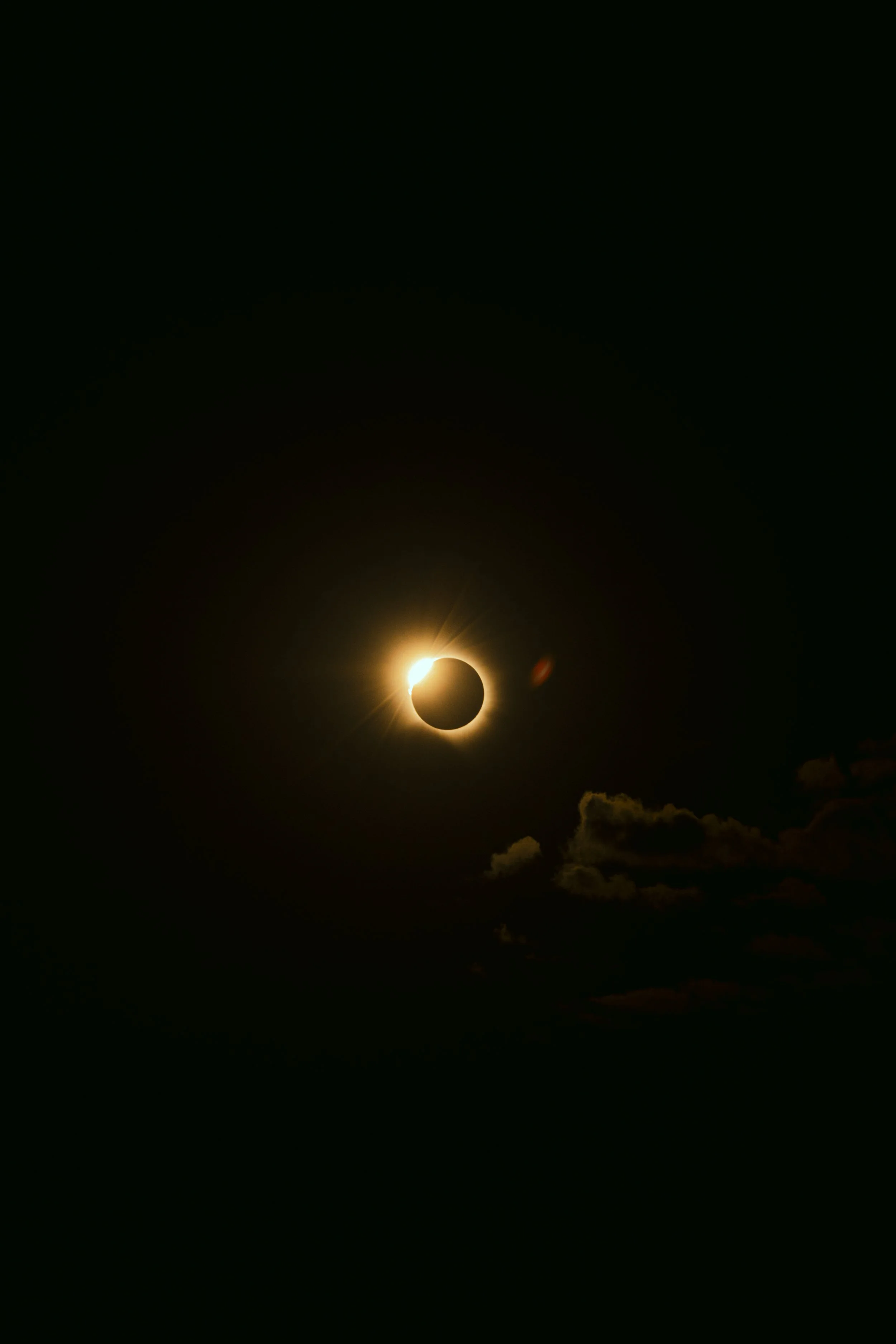 A solar eclipse occurring at night with the moon covering the sun, creating a glowing ring and a lens flare effect in the sky.