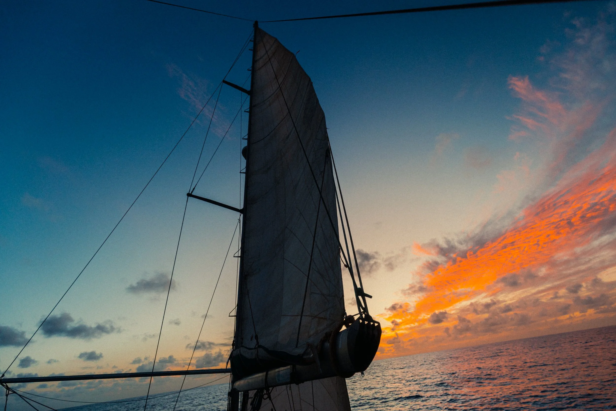 Sailboat with a large sail at sunset over the ocean, colorful clouds in the sky