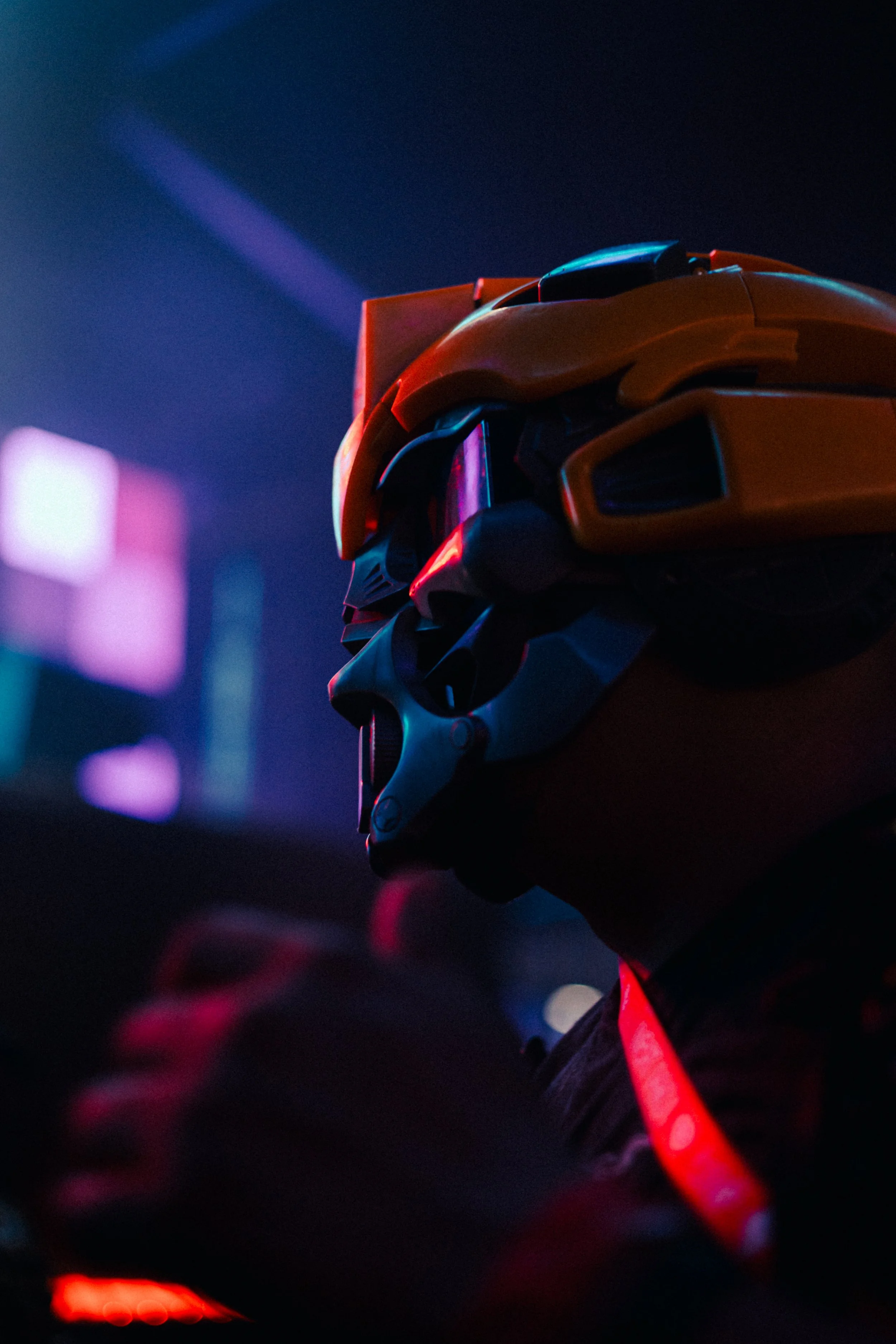 A person wearing a motorcycle helmet with a dark background illuminated by neon lights.