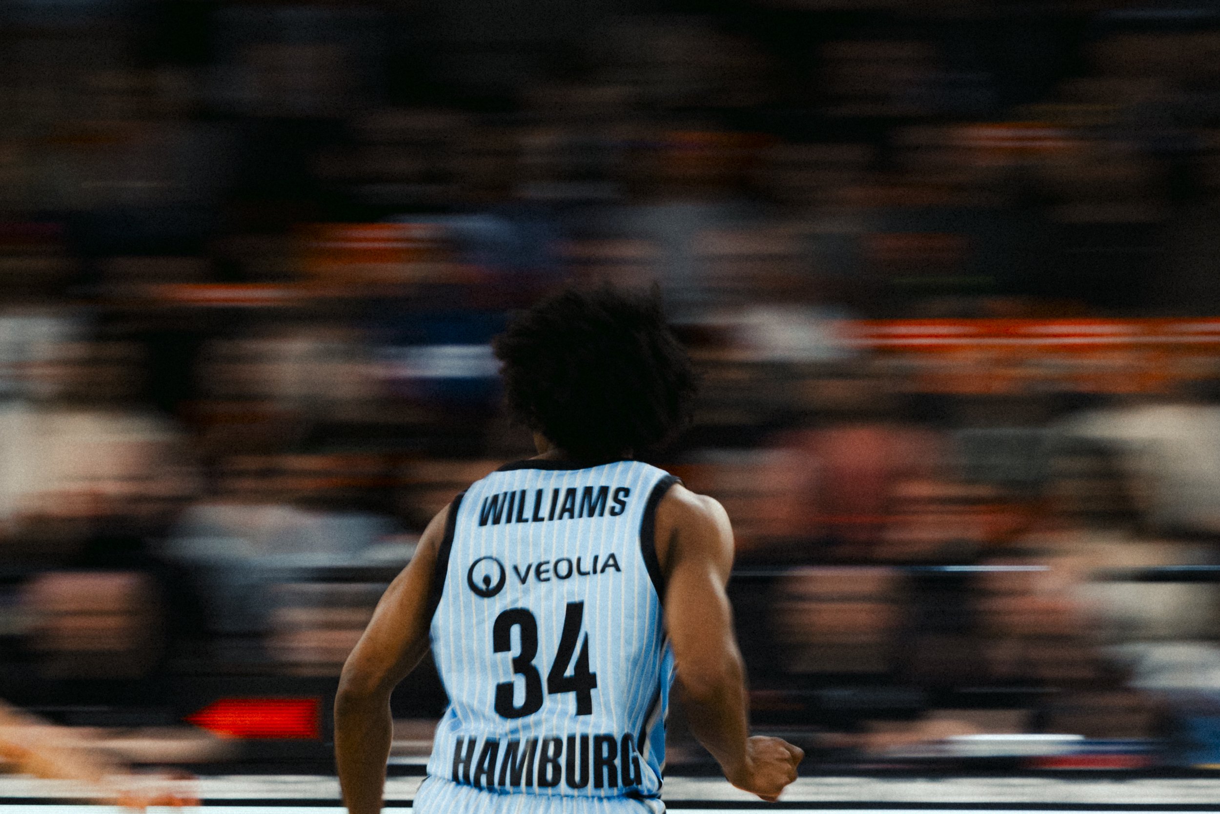 Basketball player with the last name Williams on the back of his uniform, running on the court during a game, with blurred spectators in the background.