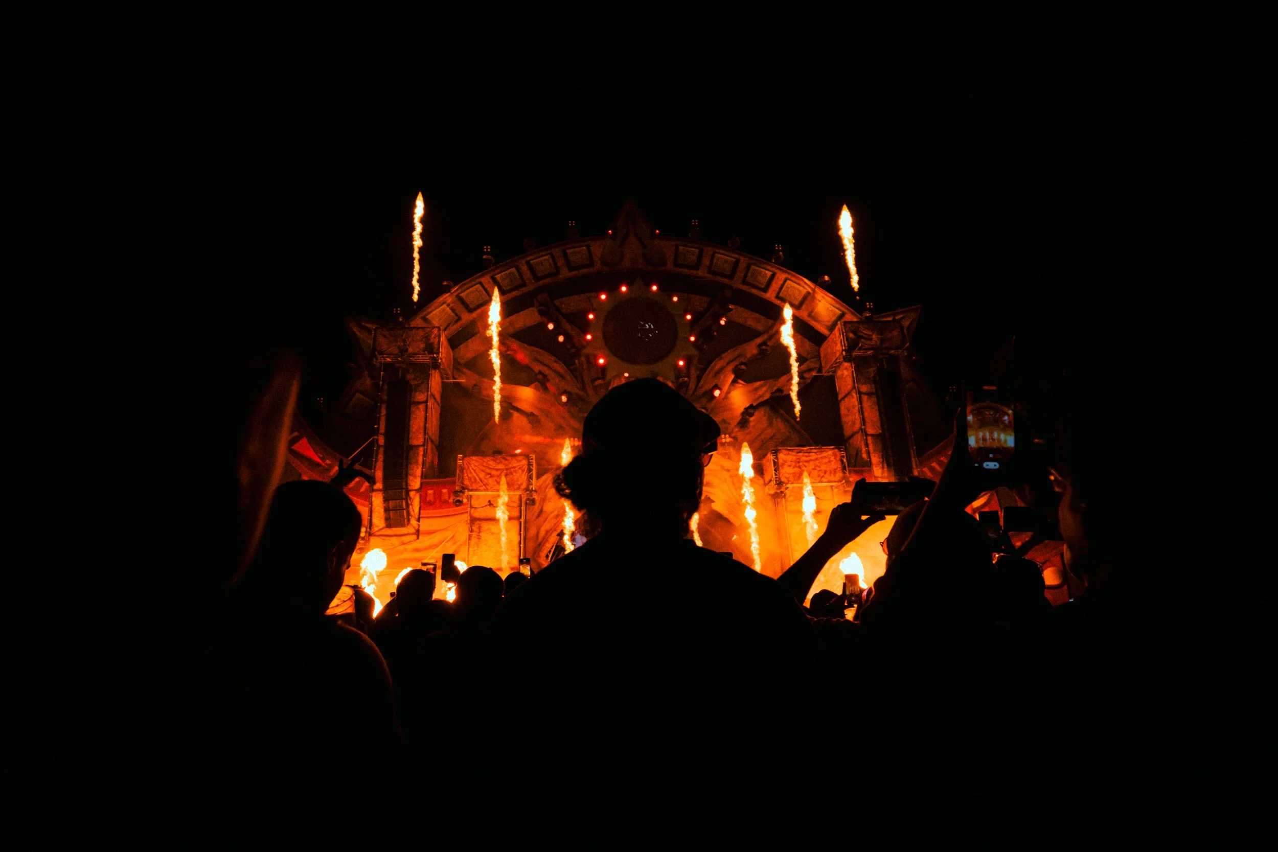 Nighttime concert stage with pyrotechnics and crowd silhouettes.