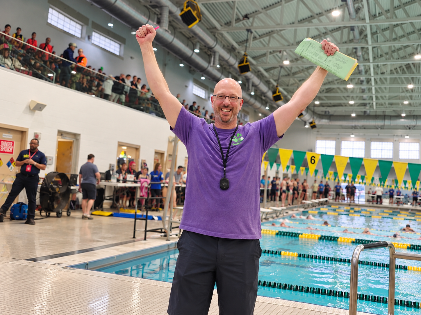 Swim coach celebrating victory with arms raised near swimmer's pool during a swim meet.