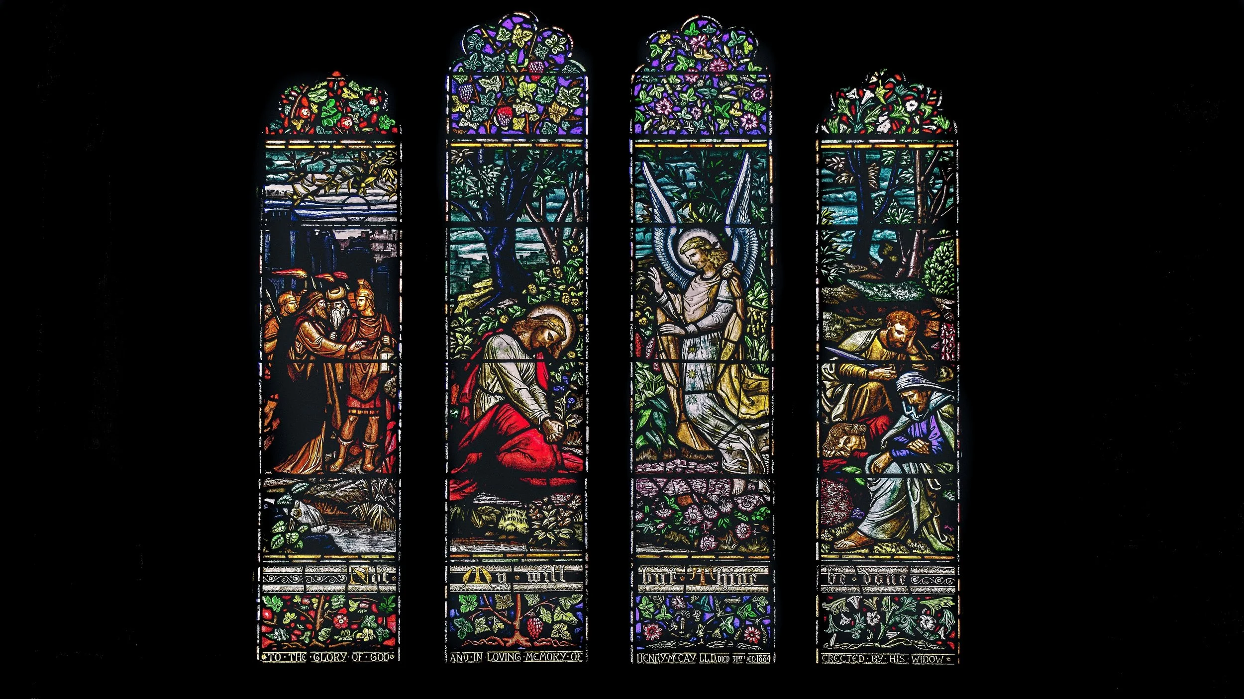 Colorful stained glass window depicting biblical scenes with floral and natural motifs.