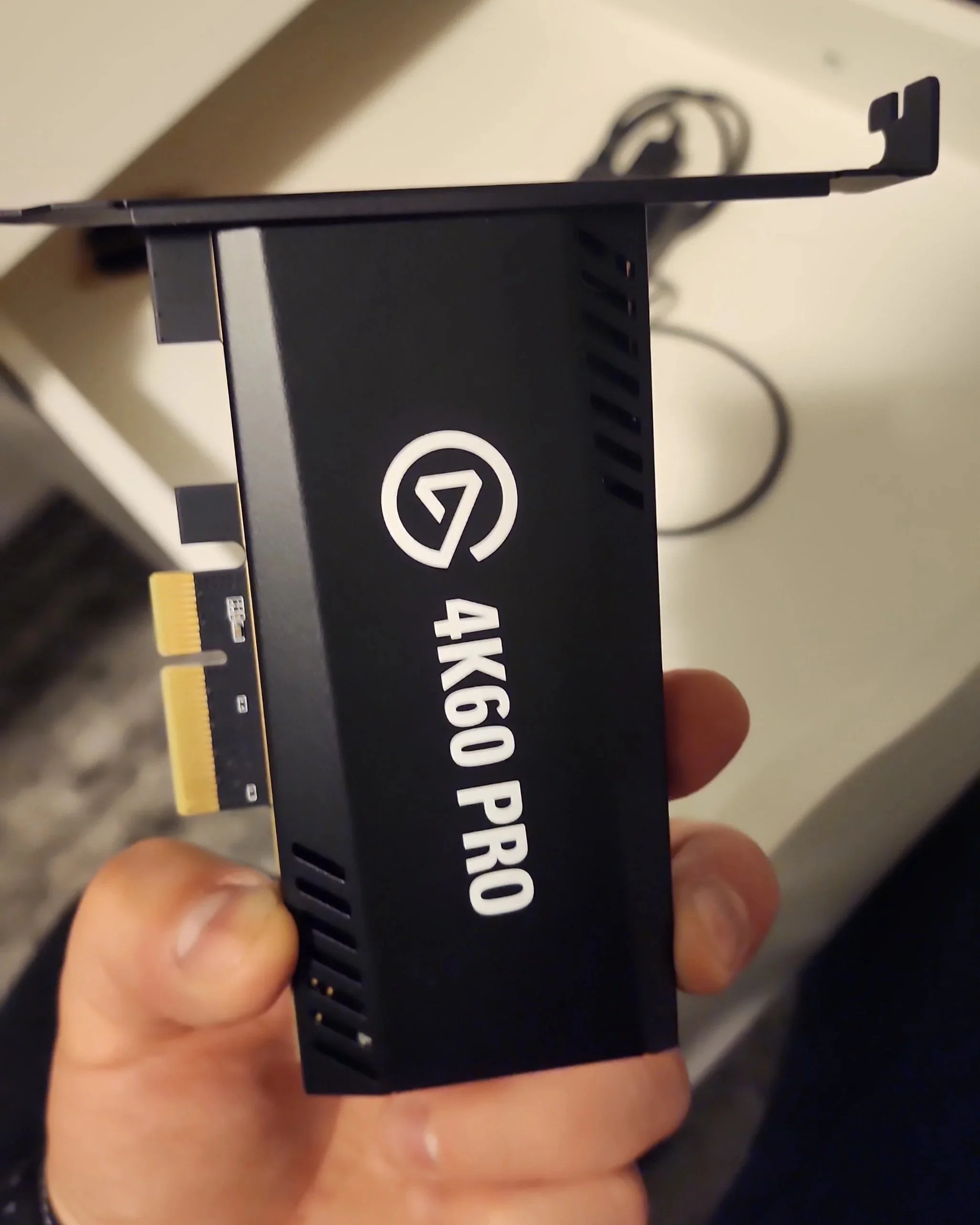A person holding a black graphics card with the label '4K60 PRO' on it, featuring a copper heat sink and venting slots.