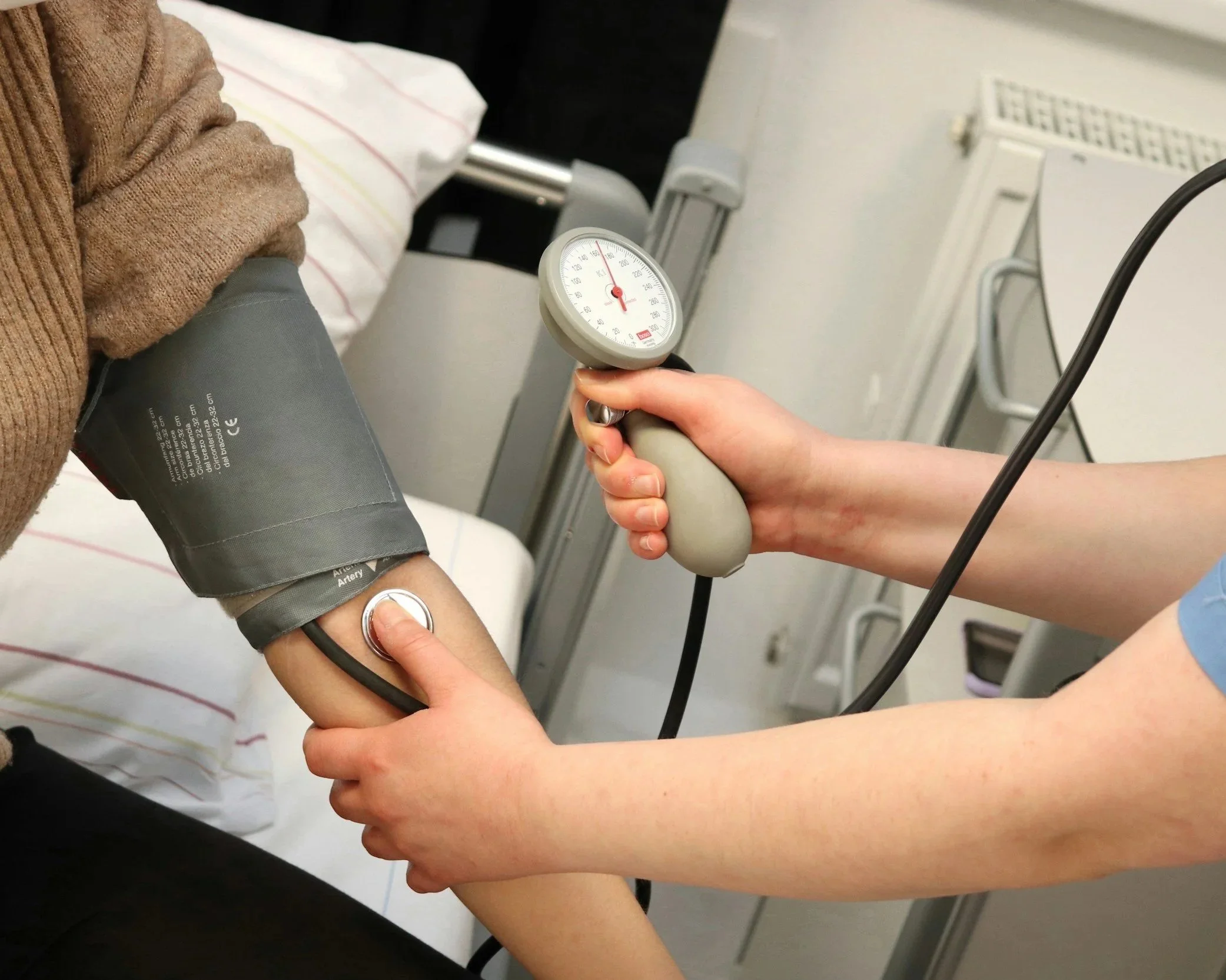 A person is getting their blood pressure checked by a healthcare professional using a sphygmomanometer, with the cuff wrapped around their arm.