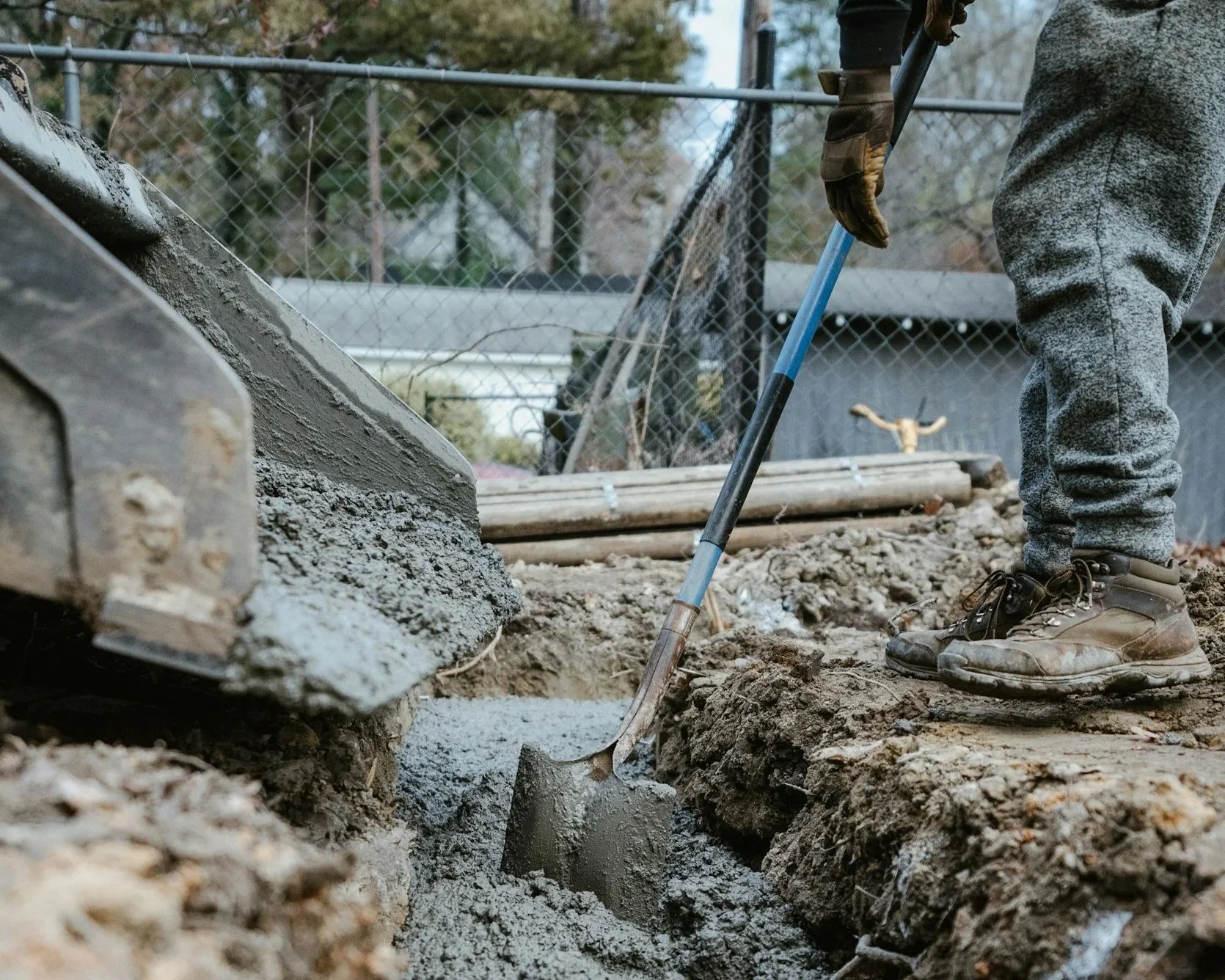 Person working on a construction site, digging a trench with a shovel, wearing gloves and work boots.