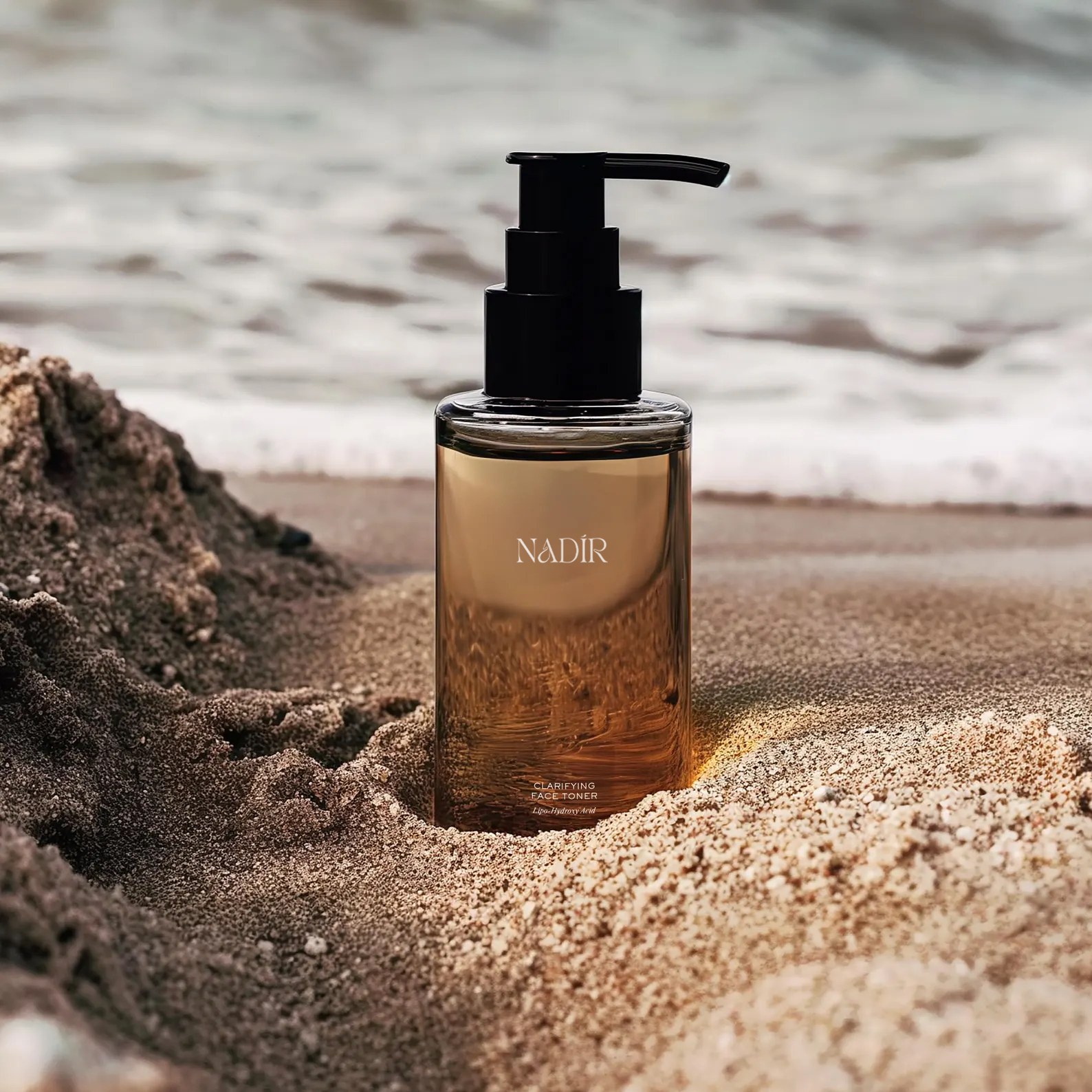 A bottle of Nadir clarifying face toner on the sand at the beach with ocean waves in the background.