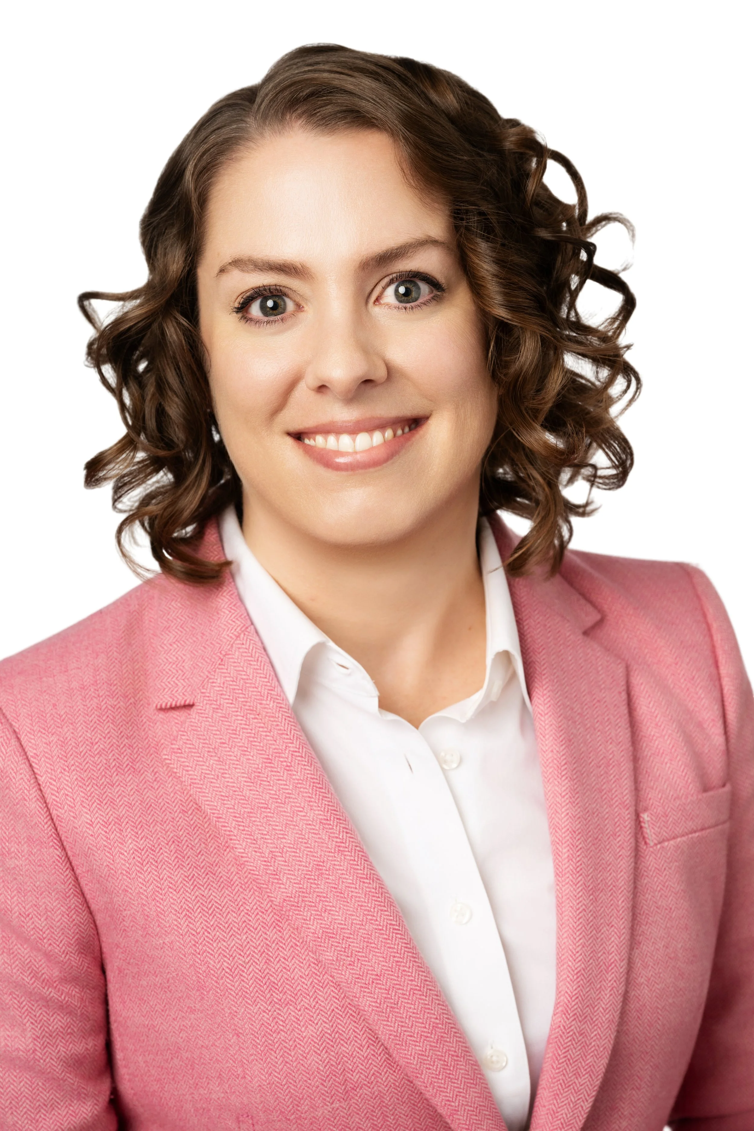 Smiling woman with curly brown hair wearing a pink blazer and white shirt